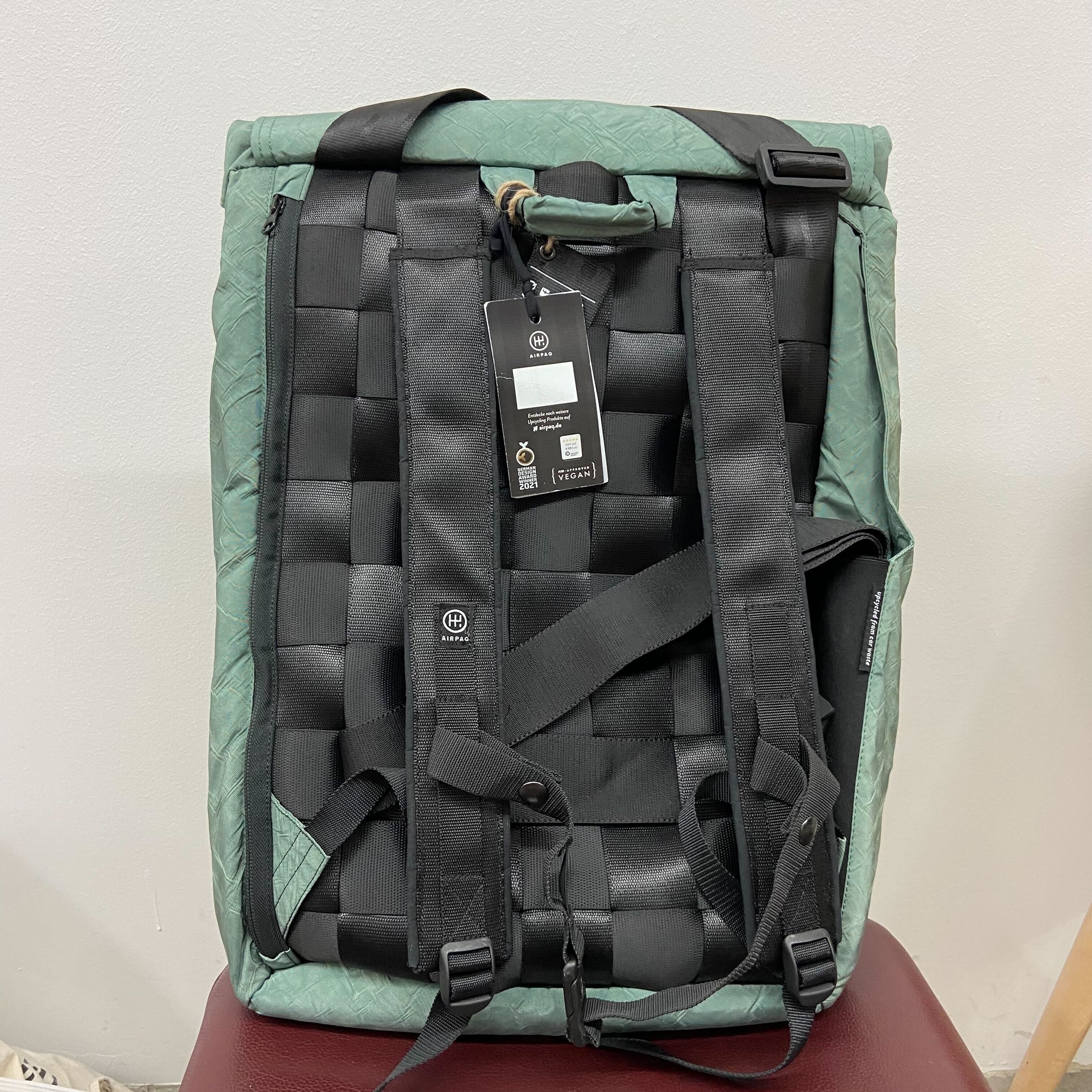 Grüner Rucksack mit schwarzen Riemen und einem Etikett, das an einem schwarzen Karabiner befestigt ist.