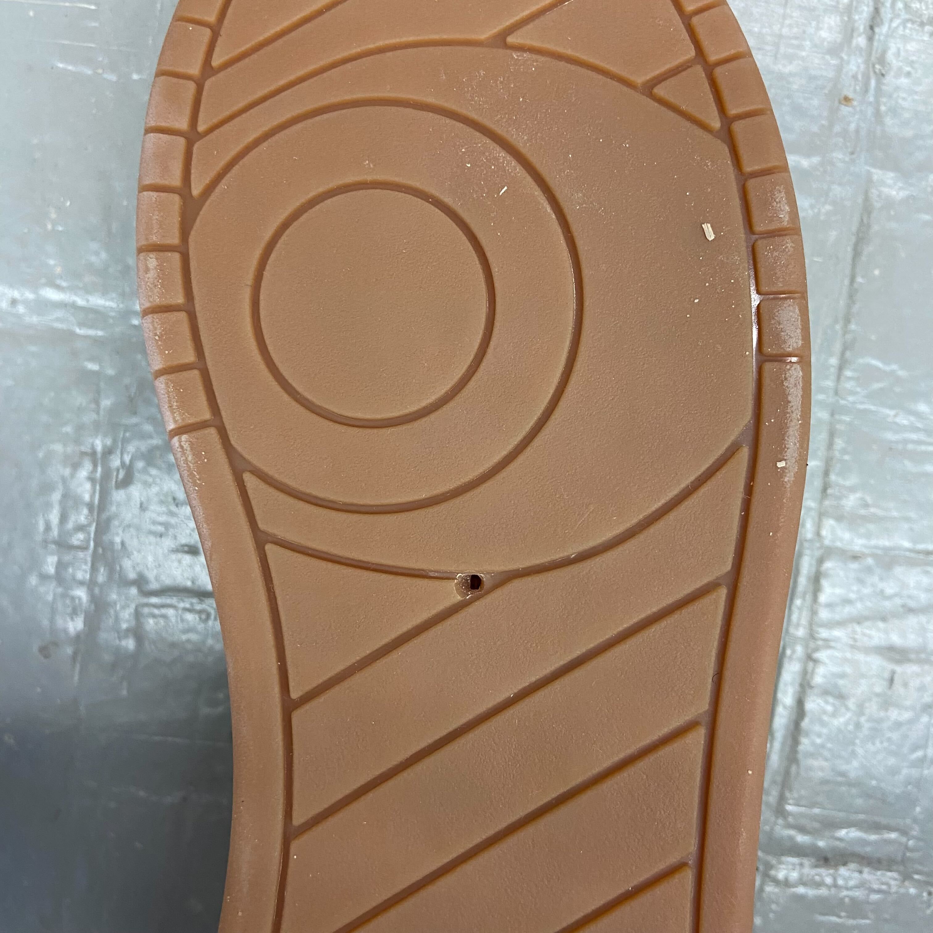 Nahaufnahme einer Schuhsohle mit kreisförmigen und diagonalen Mustern, einem kleinen Loch und etwas Schmutz.