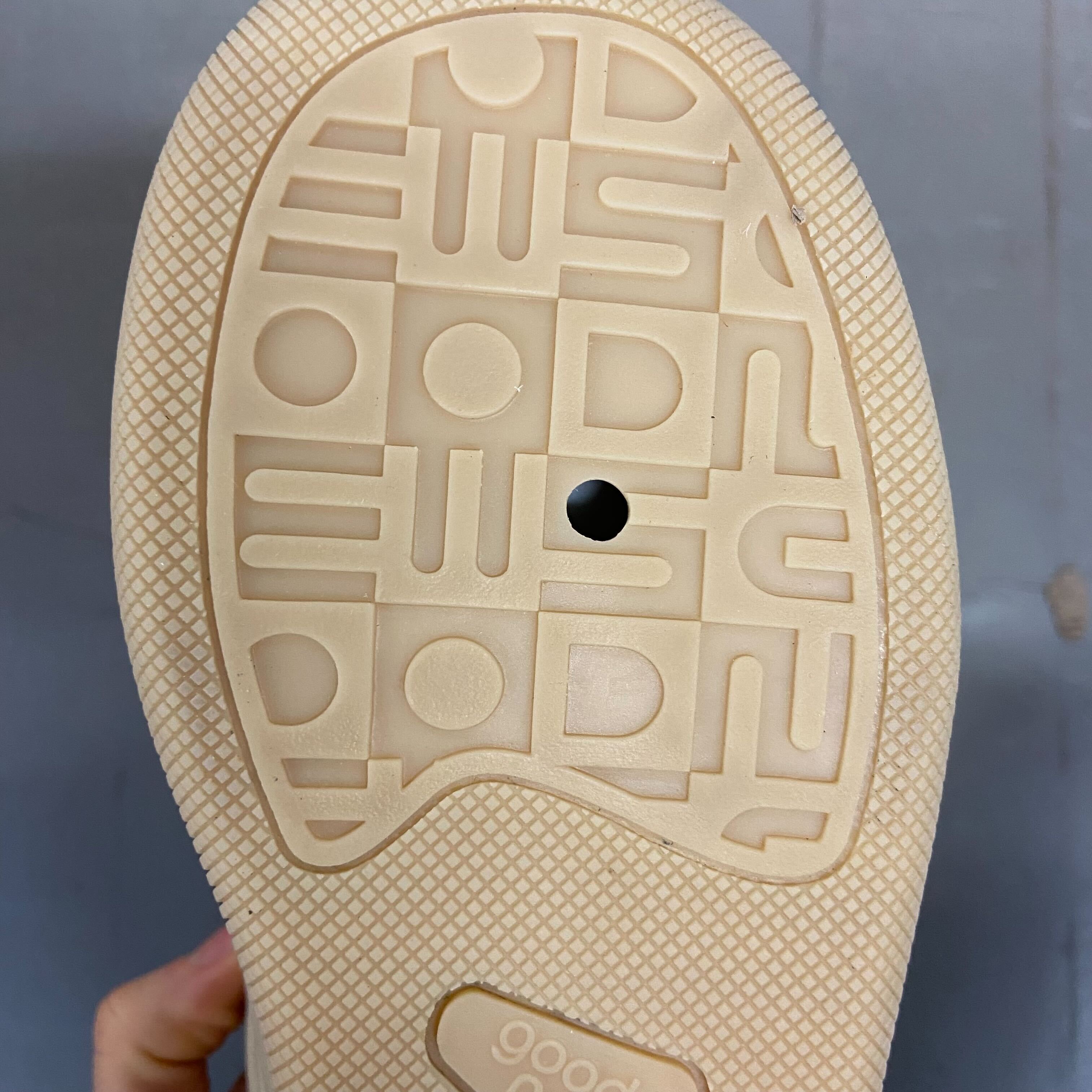 Sohle eines Schuhs mit einzigartigem Muster und einem kleinen Loch, gehalten von einer Hand.