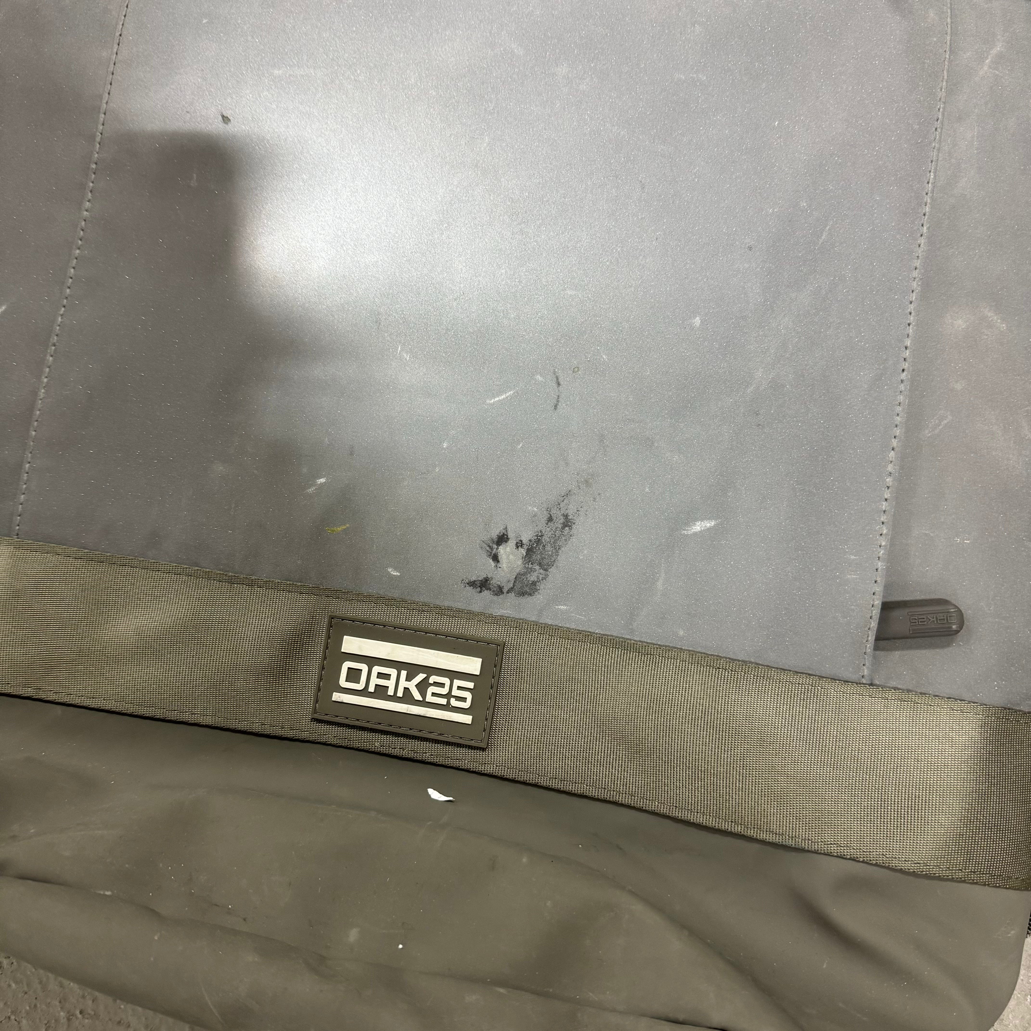 Grauer Stoff mit dem Logo "OAK25", sichtbar ist ein leichter Fleck und eine strukturierte Kante.