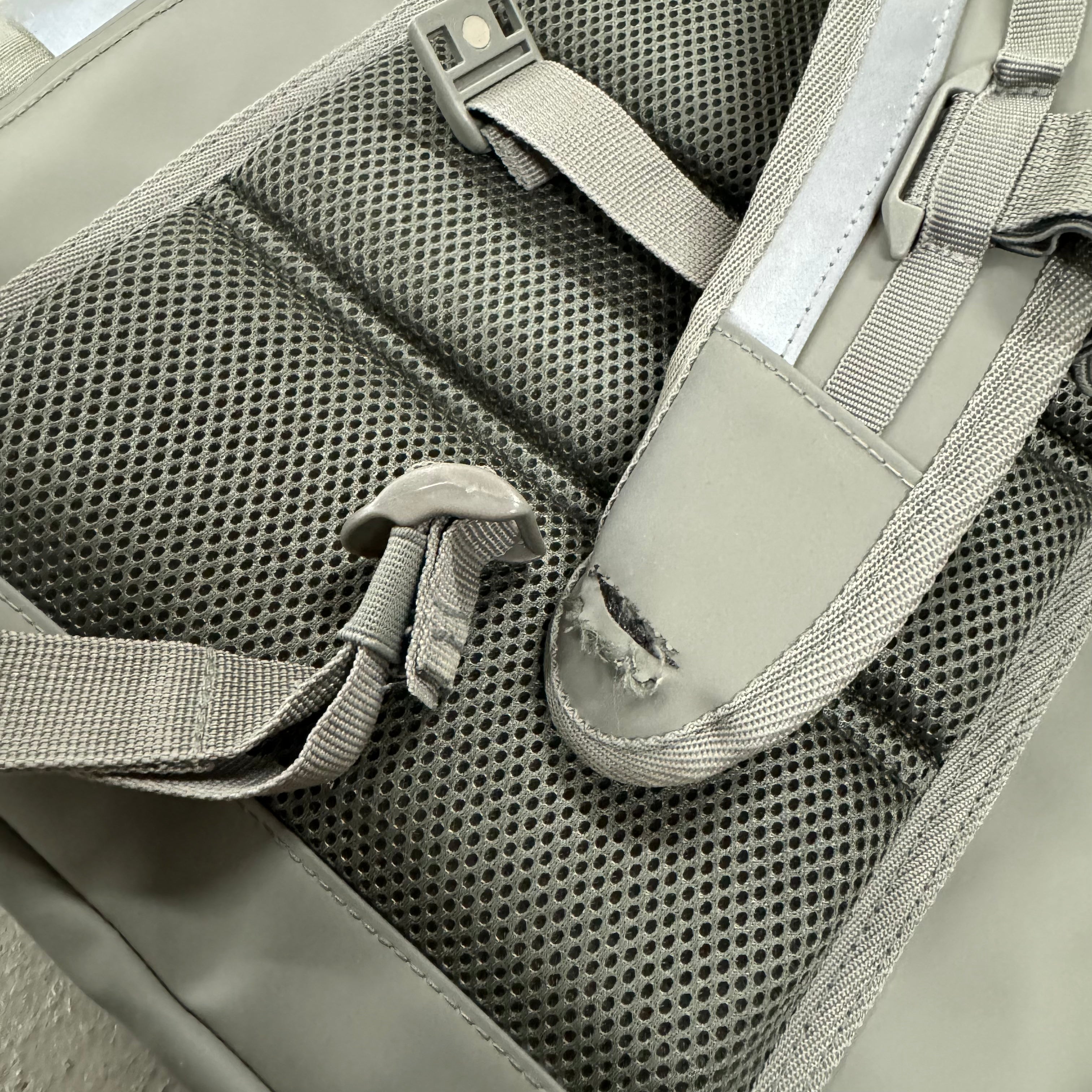 Rückseite eines Rucksacks mit gepolstertem Mesh und einem beschädigten Riemen.