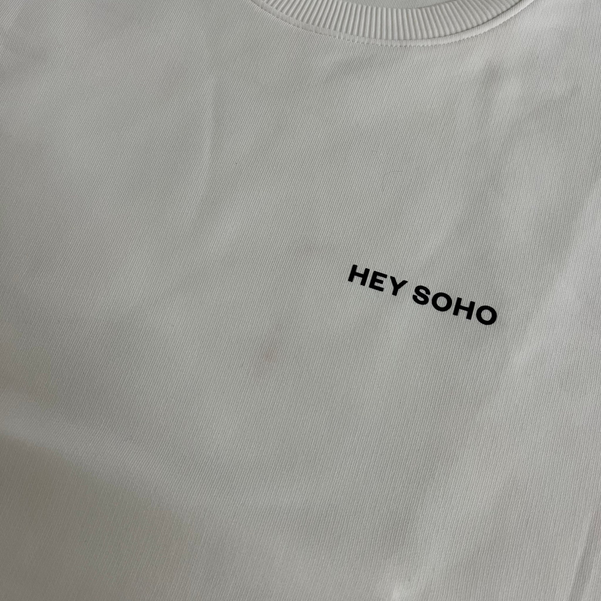 Weißes Oberteil mit dem Text "HEY SOHO" in schwarzer Schrift auf der linken Seite.