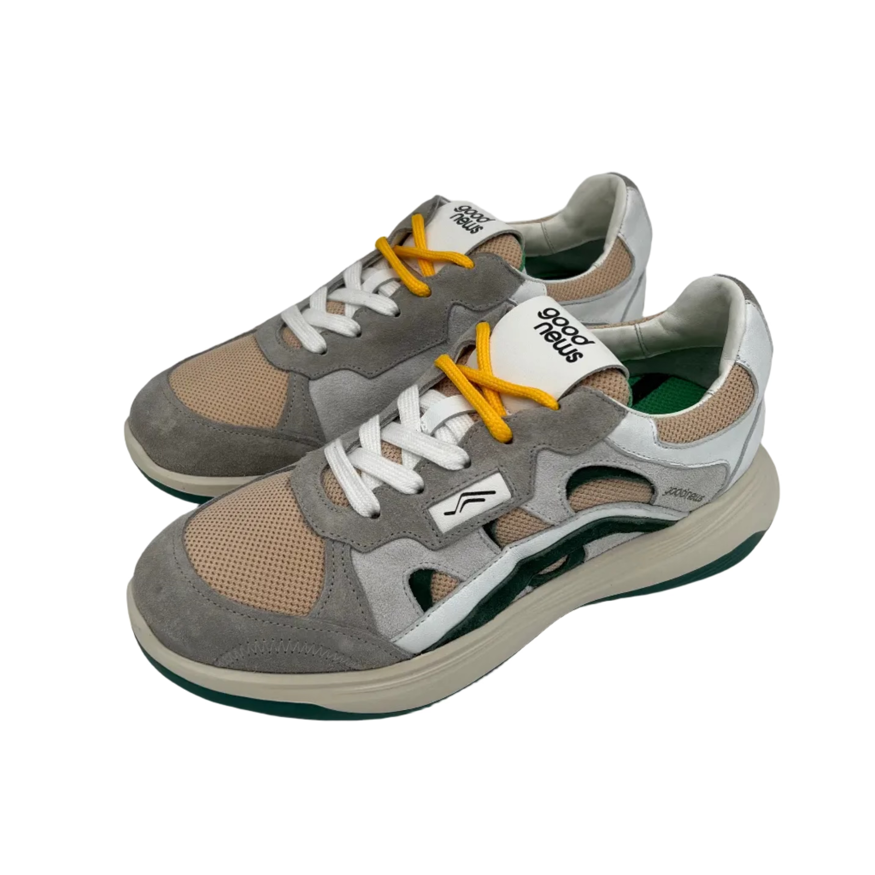 Ein Paar stylische Sneaker mit grauen, beigen und weißen Einsätzen, gelben Schnürsenkeln und einer dicken weißen und grünen Sohle. Die Schuhe sind aus Mesh und Wildleder gefertigt und haben ein Good News Branding auf der Zunge.