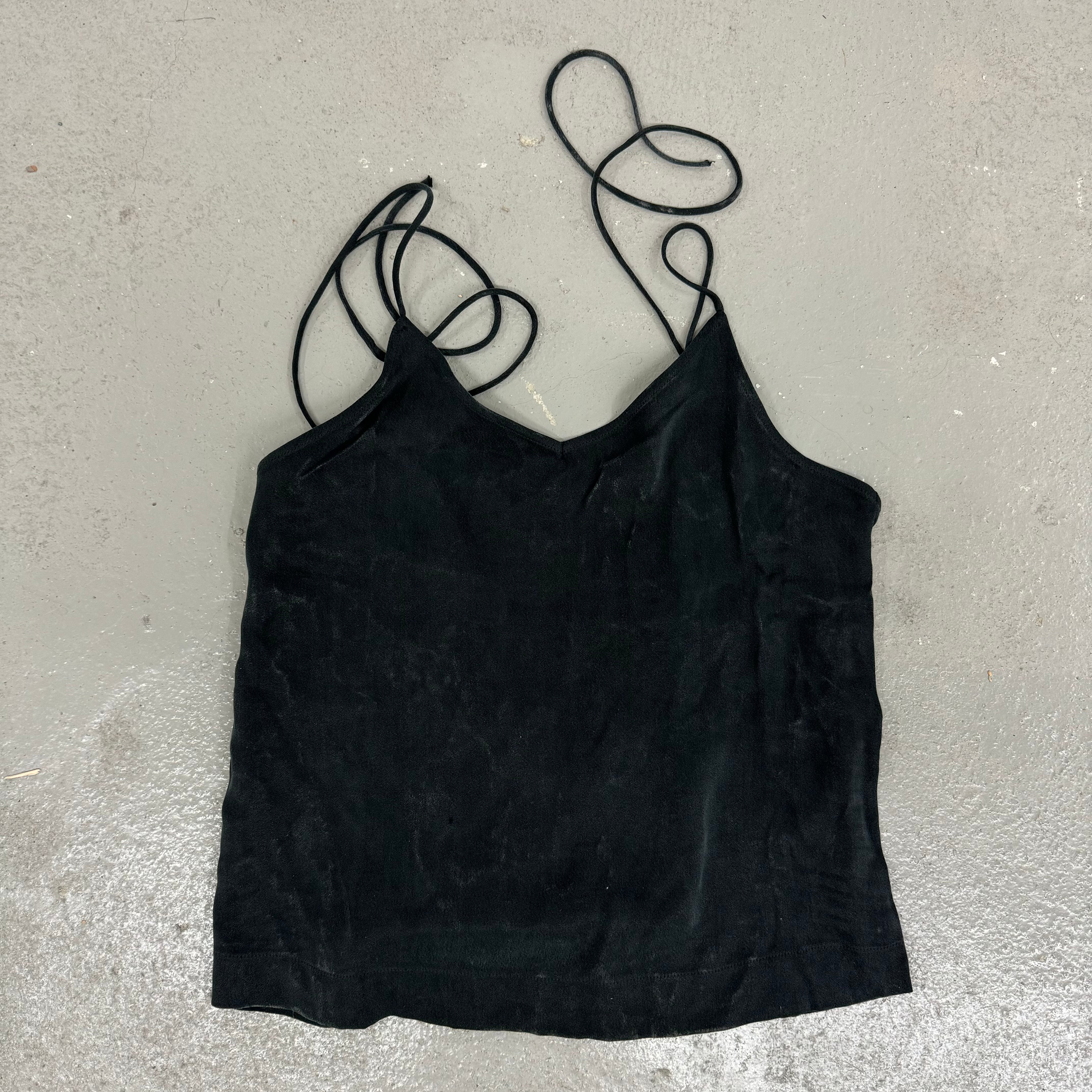 Schwarzes Trägertop mit dünnen Bändern liegt flach auf einem grauen Untergrund.