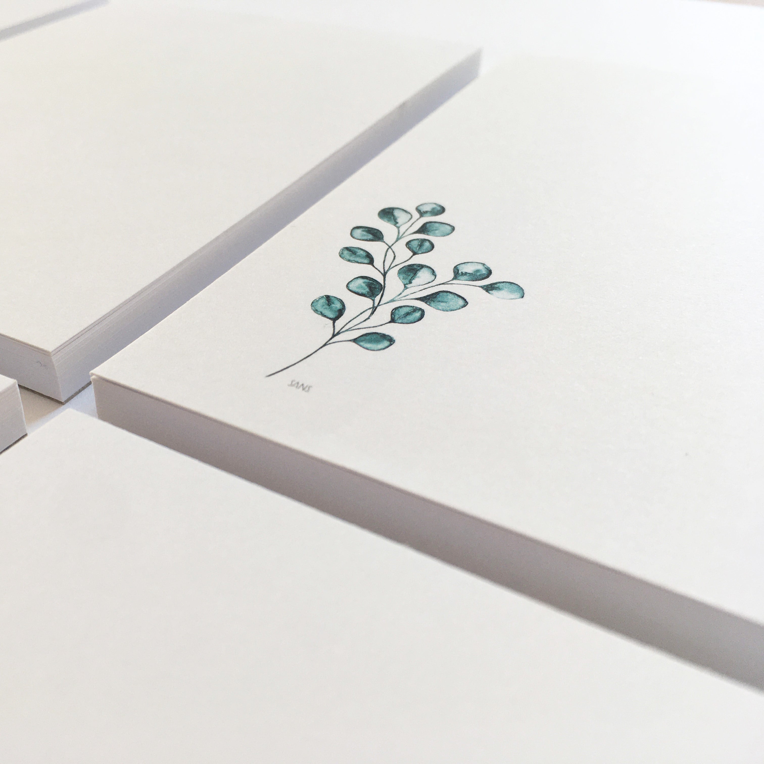 Stapel weiße Notizblöcke mit einem gezeichneten grünen Zweig auf dem vordersten Block.