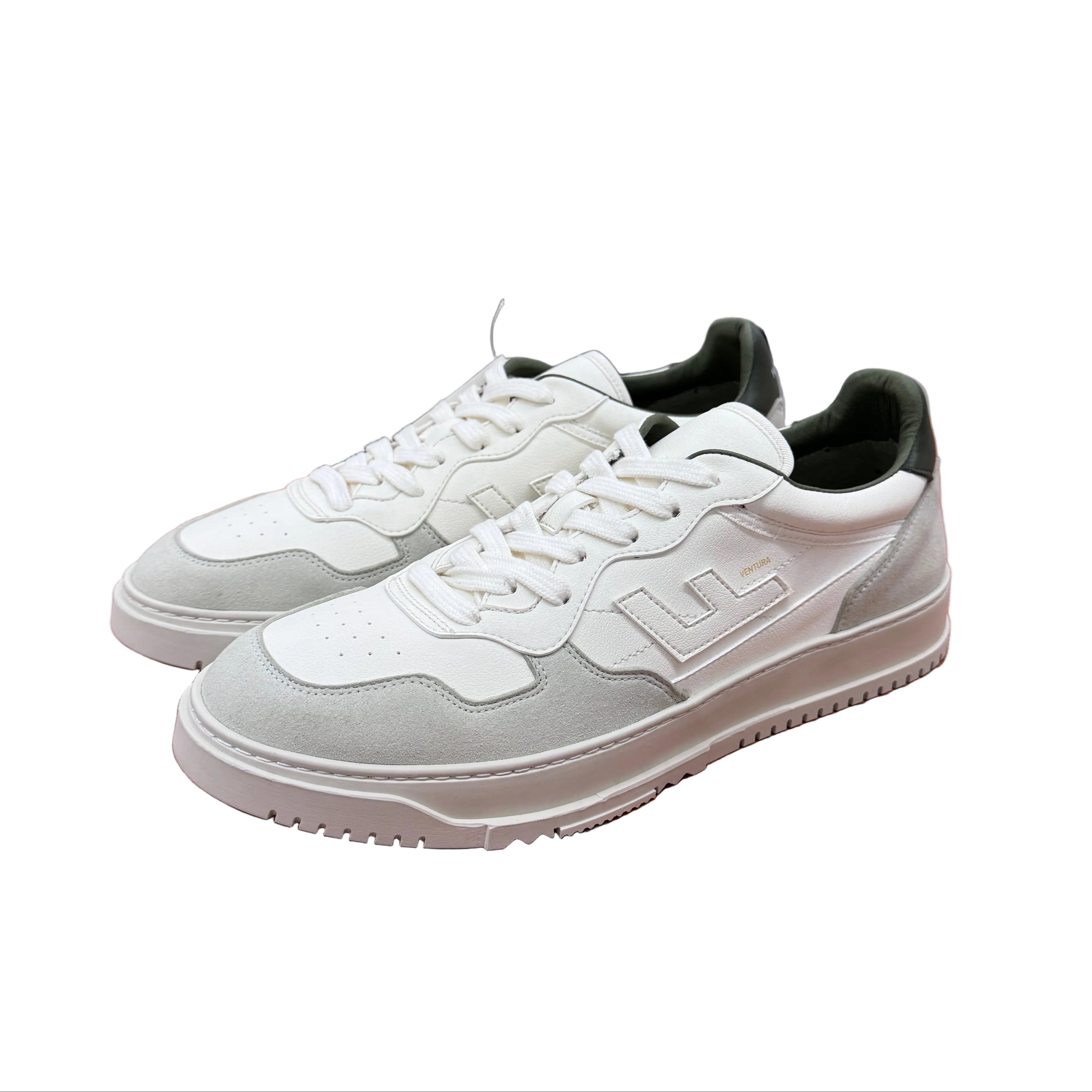 Ein Paar weiße Turnschuhe mit dunkelgrünen Akzenten und LL-Logo an der Seite, die auf einem Holztisch in einem geräumigen, modernen Studio platziert sind.