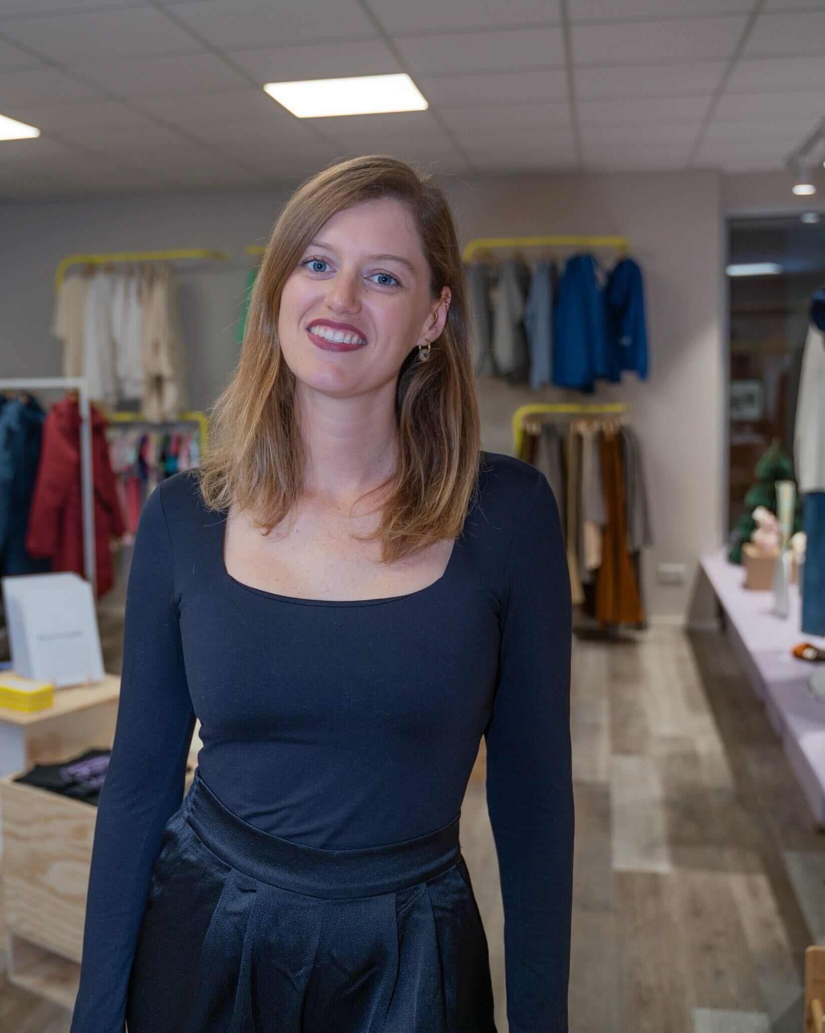 Frau in schwarzem Oberteil steht lächelnd in einem Bekleidungsgeschäft.