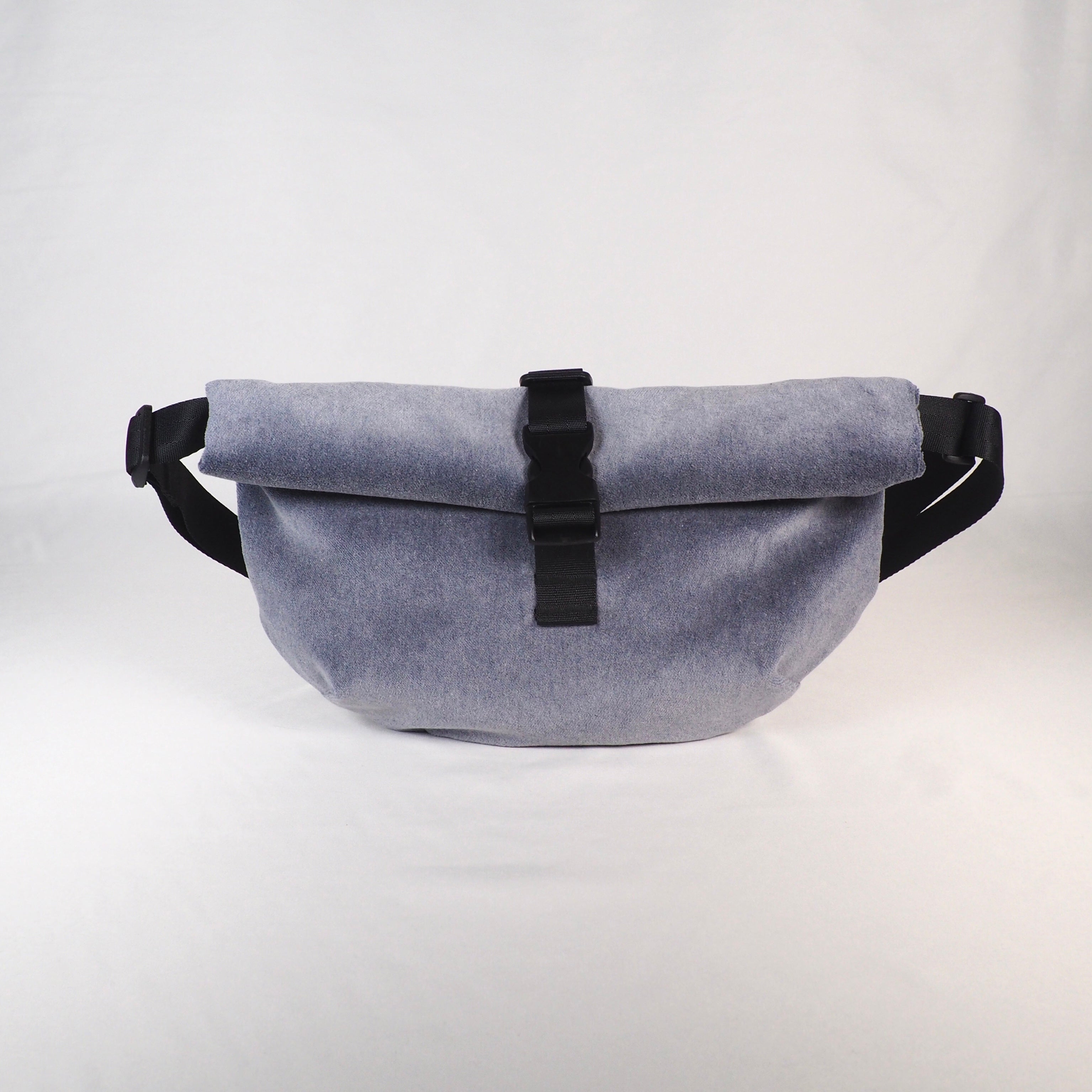 Graue Umhängetasche mit schwarzem Verschluss und Gurt auf weißem Hintergrund.