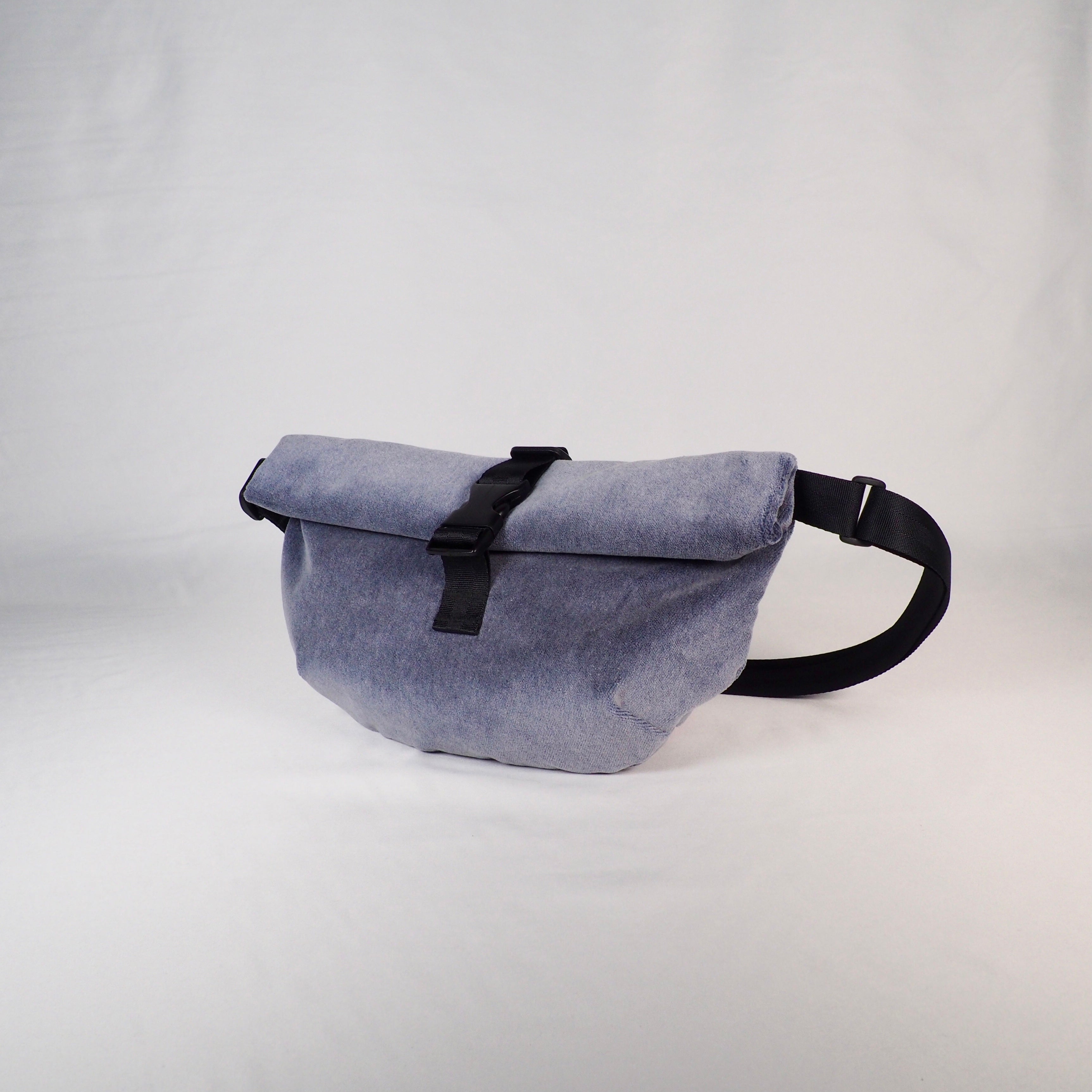 Graue Umhängetasche mit schwarzem Gurt und Schnalle, auf neutralem Hintergrund fotografiert.