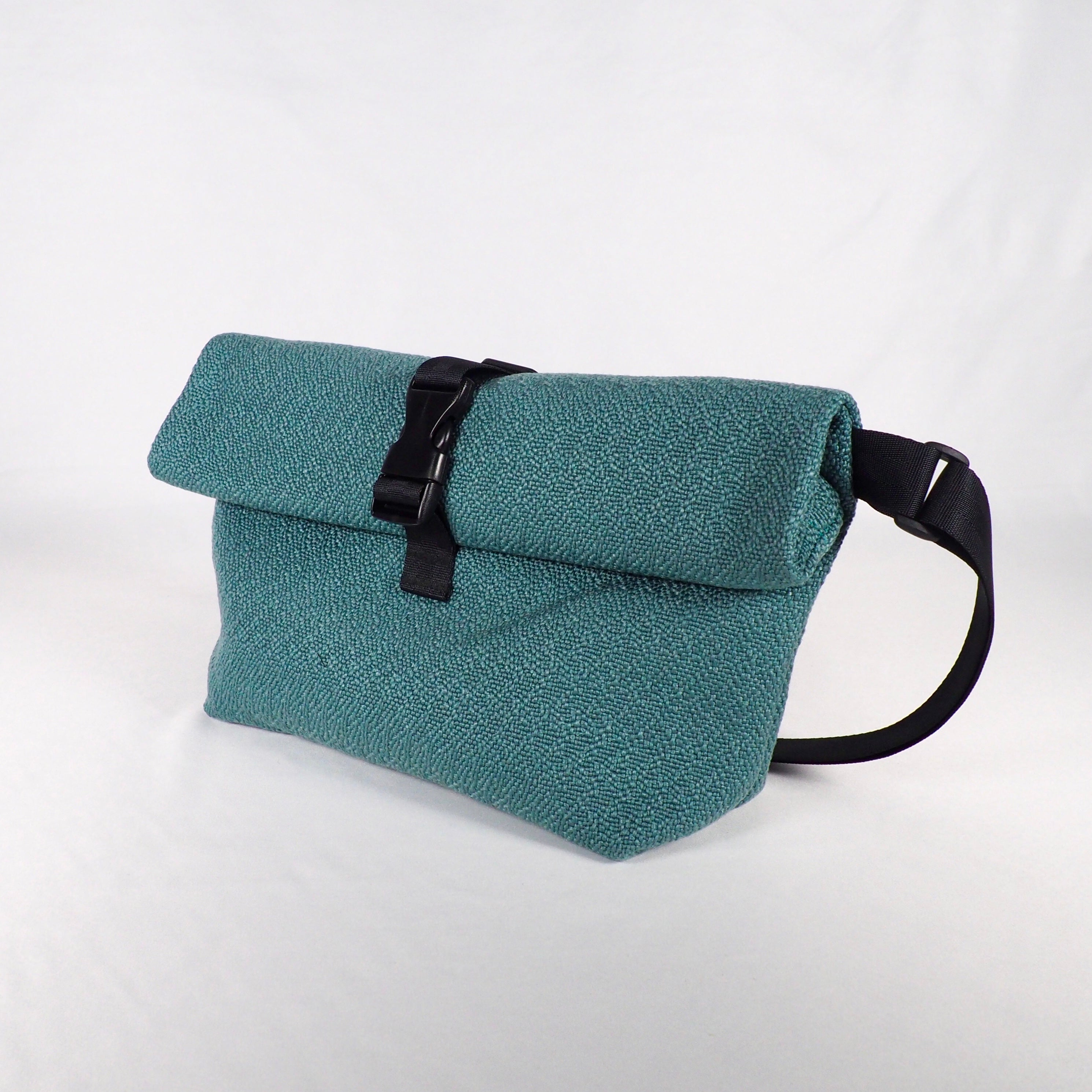 Eine türkisfarbene Umhängetasche mit schwarzem Verschluss und Riemen vor einem weißen Hintergrund.