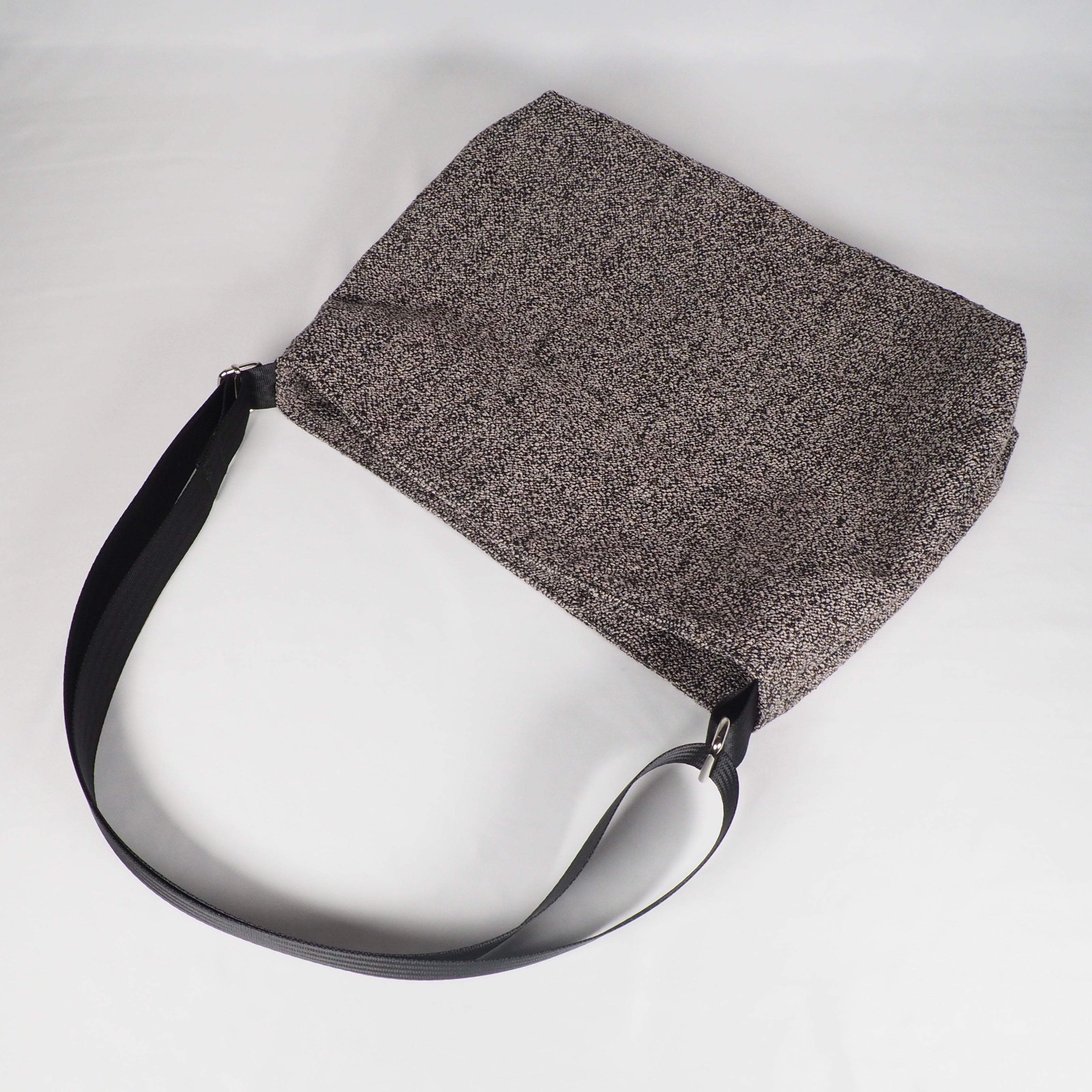 Graue Schultertasche vor weißem Hintergrund.