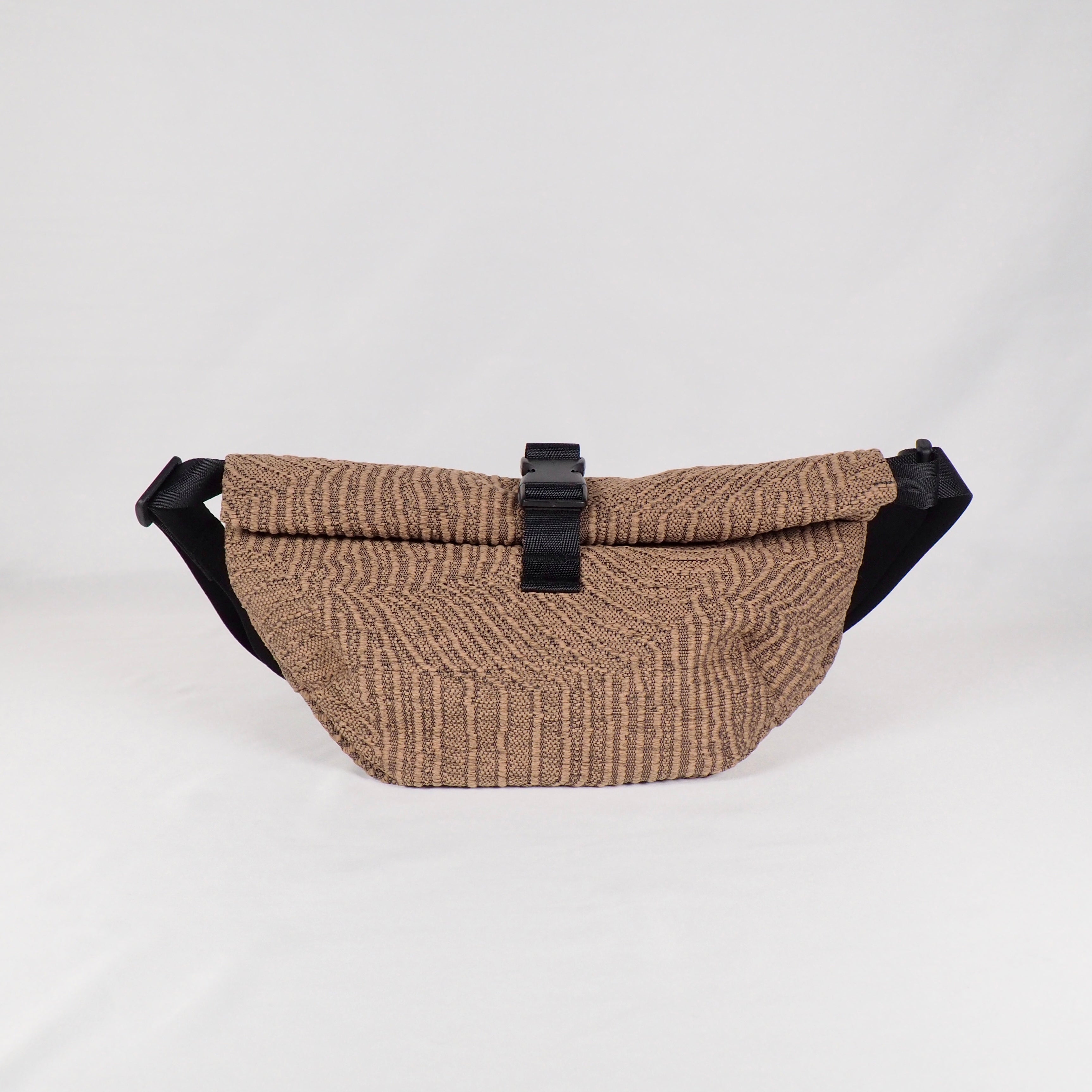 Beige Gürteltasche mit strukturiertem Muster und schwarzem Verschluss auf weißem Hintergrund.