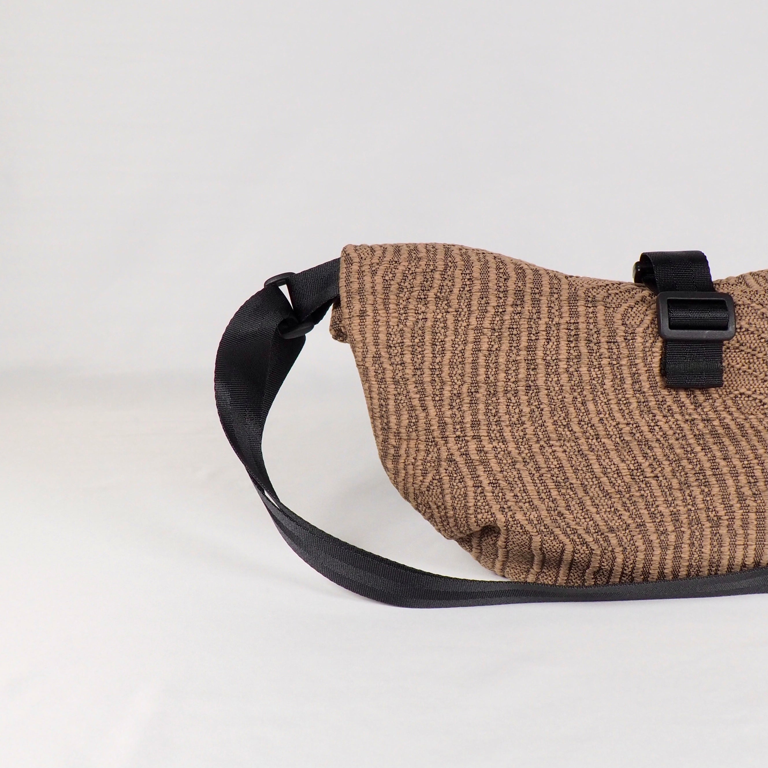 Braune, gestreifte Tasche mit schwarzem Riemen und Schnalle auf weißem Hintergrund.