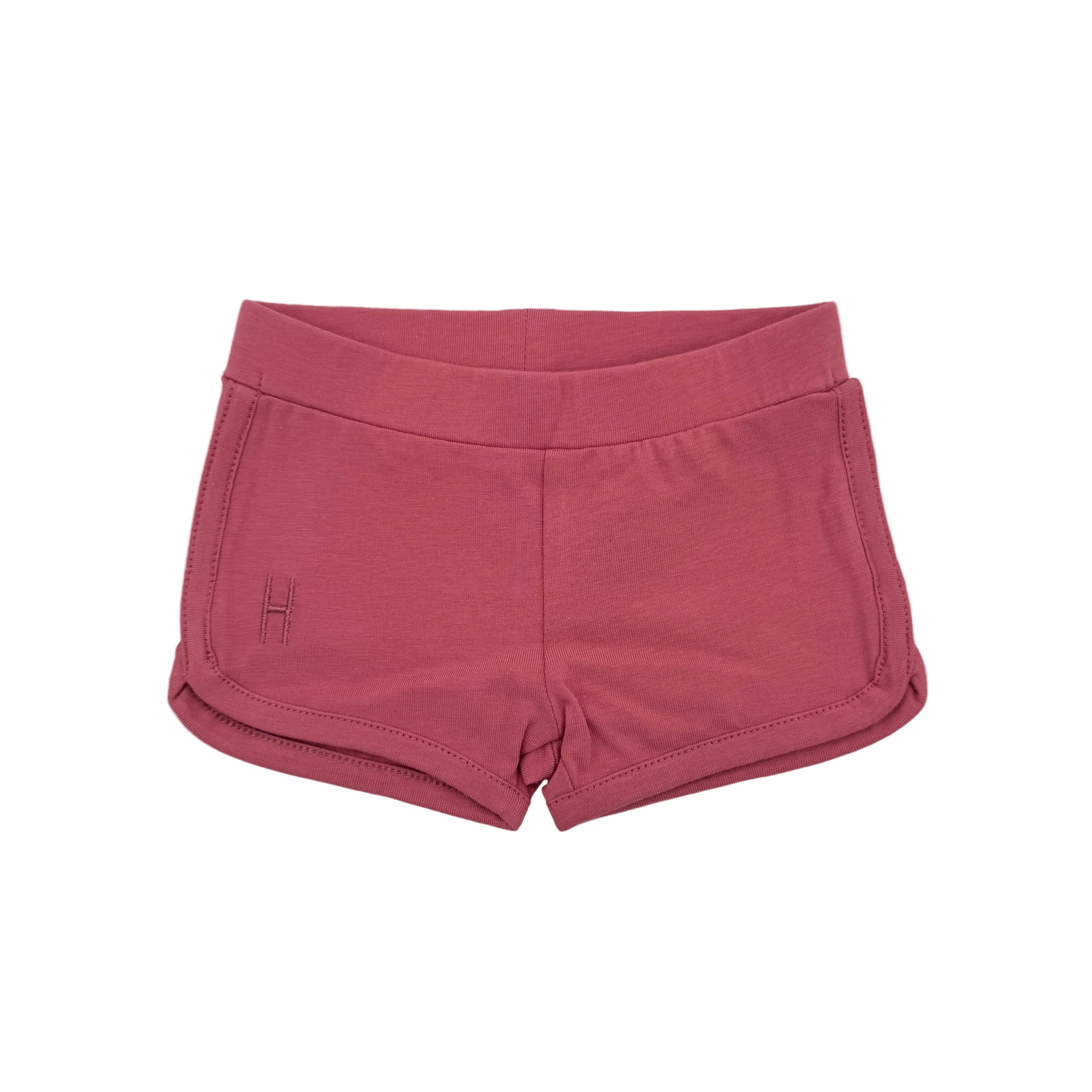 Pinkfarbene Sportshorts mit elastischem Bund und abgerundetem Saum, die für Komfort und Bewegungsfreiheit sorgen. Die Shorts haben minimale Nahtdetails und ein kleines gesticktes Logo auf der linken Seite.