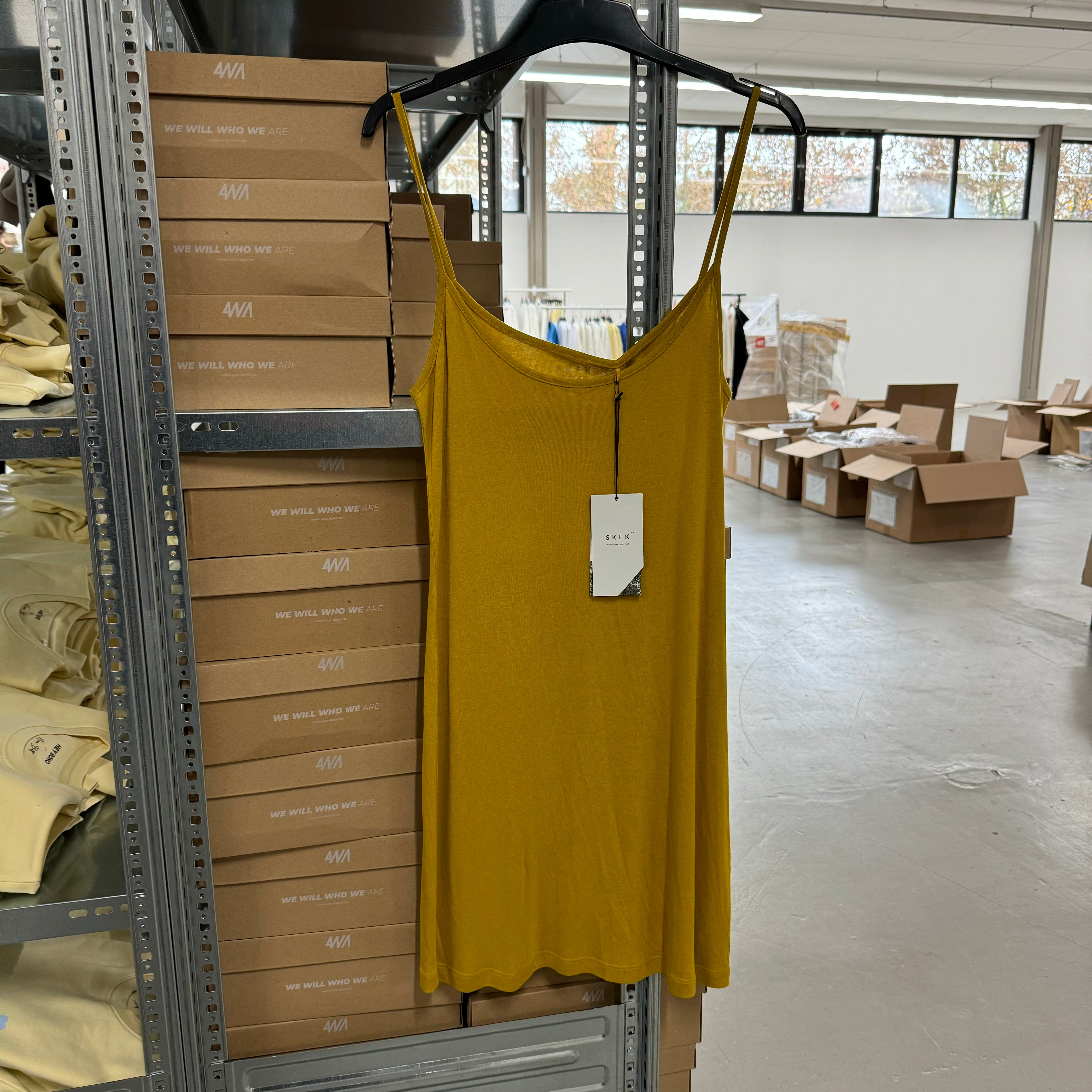Gelbes Kleid auf Kleiderbügel vor Regalen mit Kartons in einem Lagerraum.