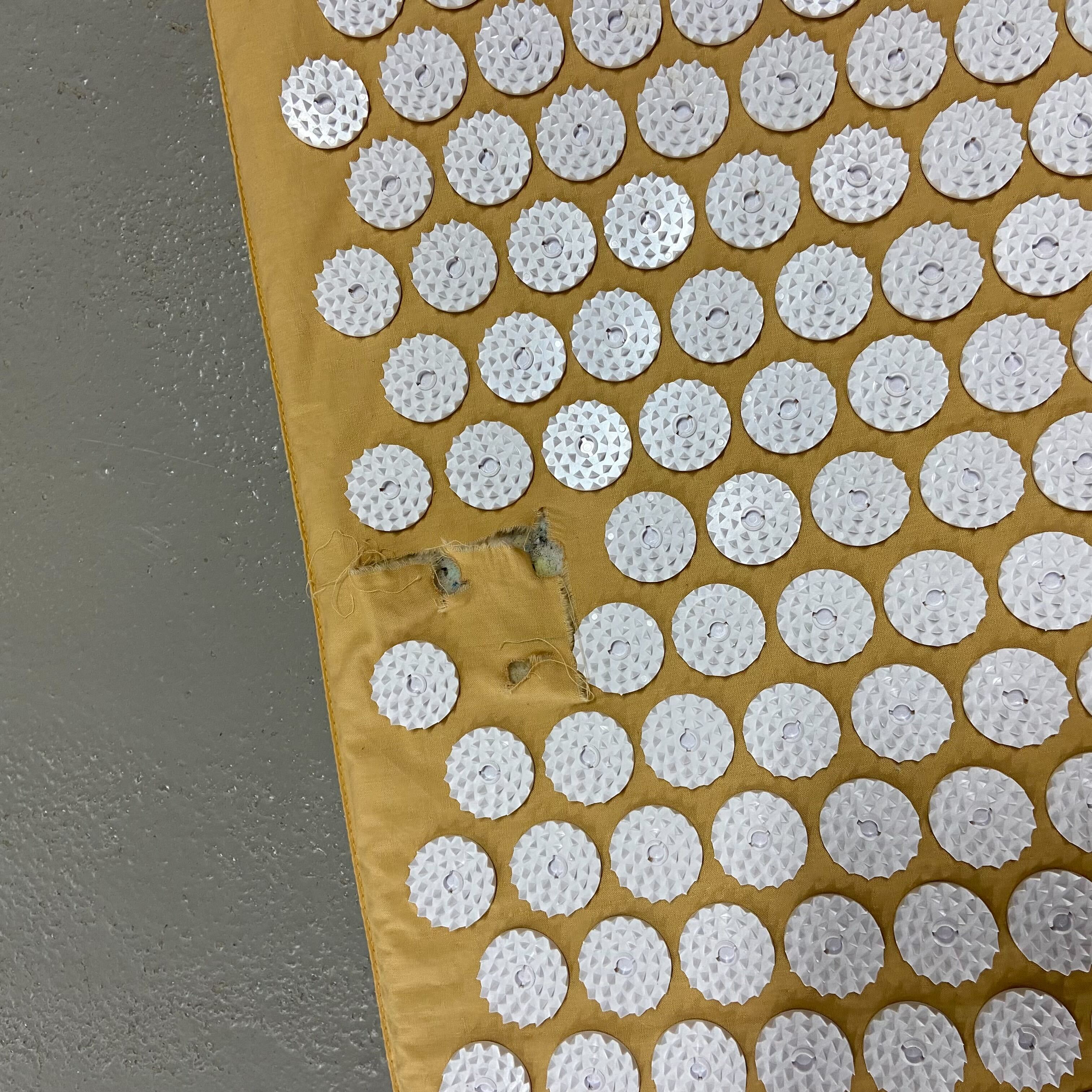 Gelbe Matte mit vielen weißen, runden Akupressurpads, einige mit Löchern in der Mitte und Stoffbeschädigung am Rand.