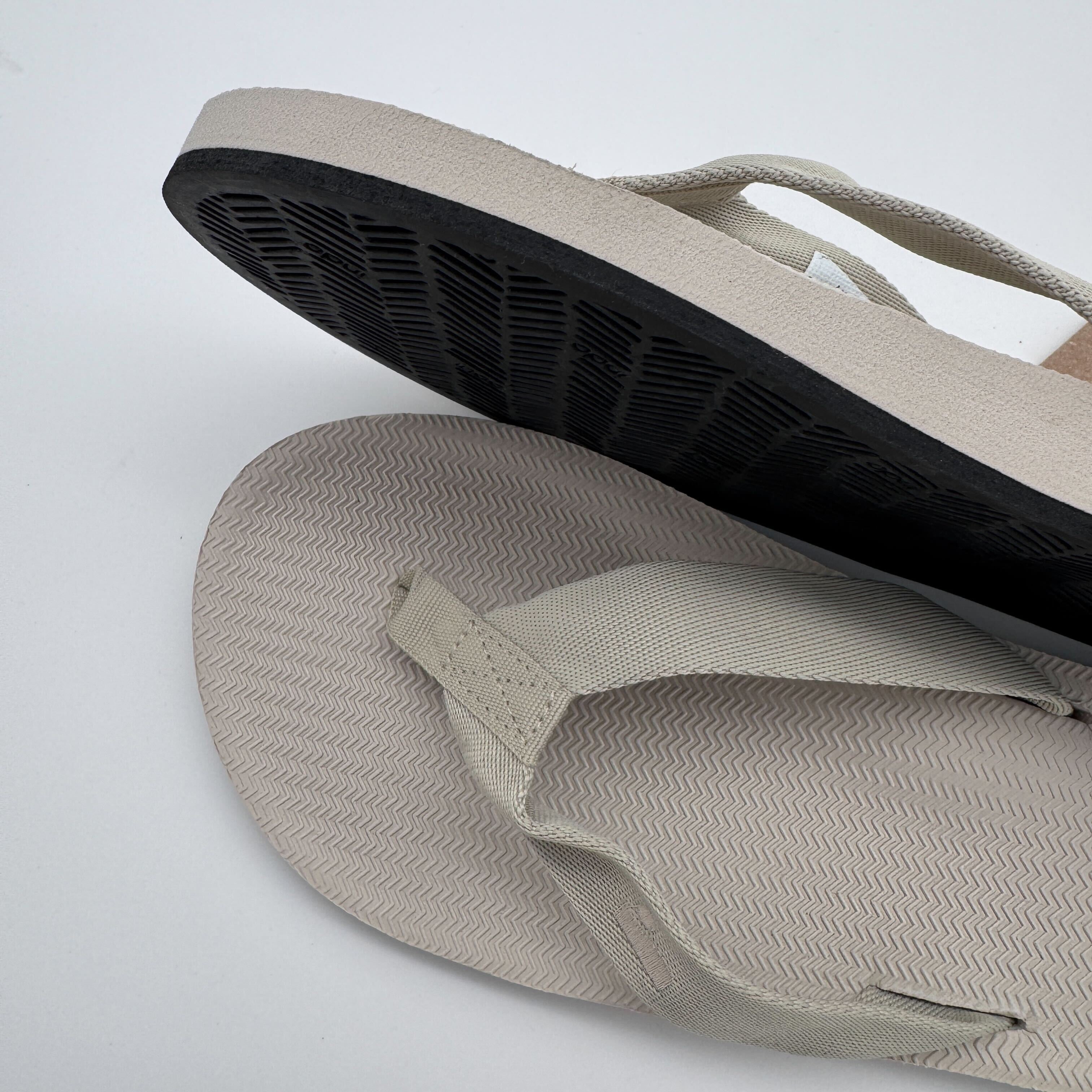 Beige Flip-Flops auf weißem Hintergrund, einer zeigt die Sohle, der andere die Oberseite mit Riemen.