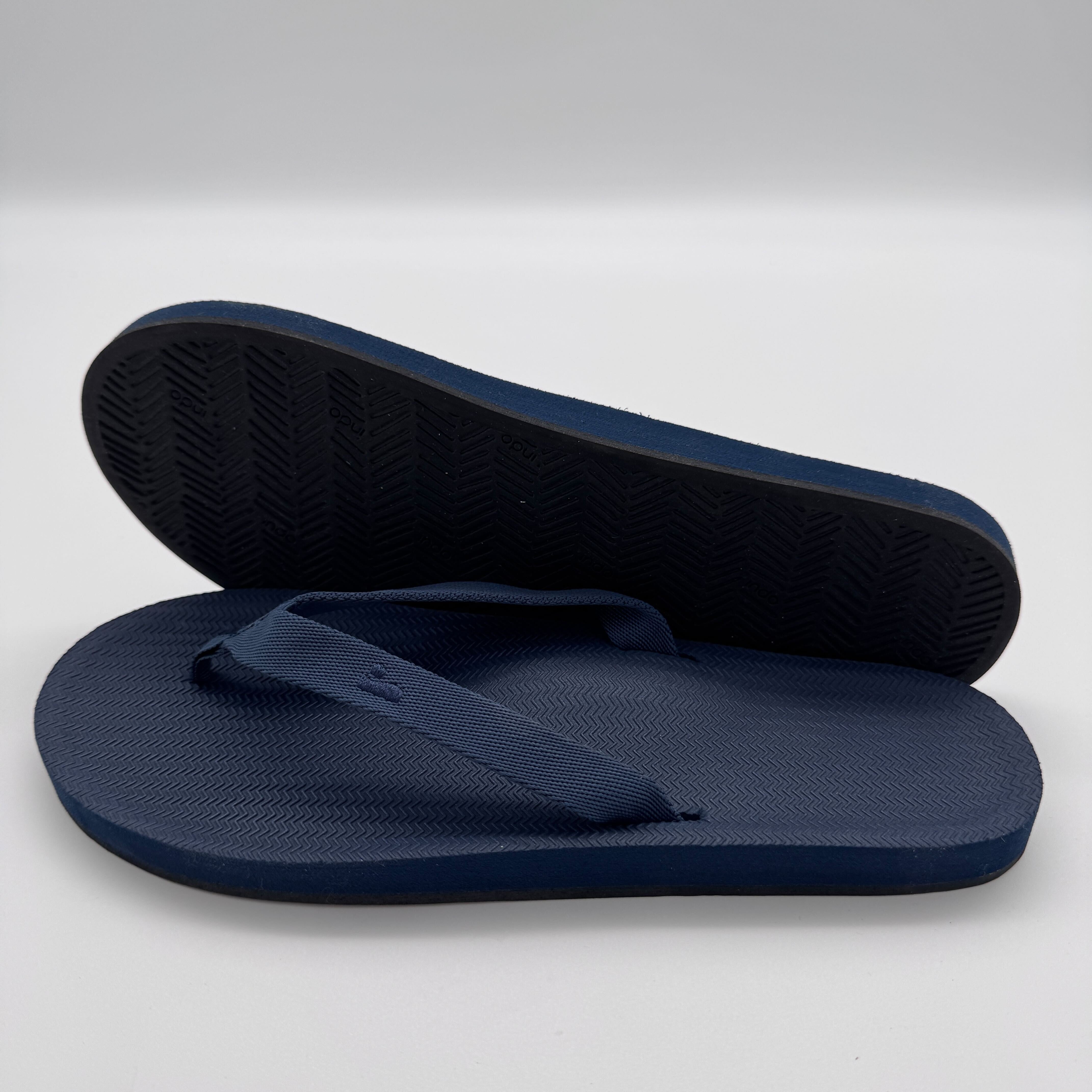 Dunkelblaue Flip-Flops, eine steht aufrecht, die andere liegt flach, auf weißem Hintergrund.
