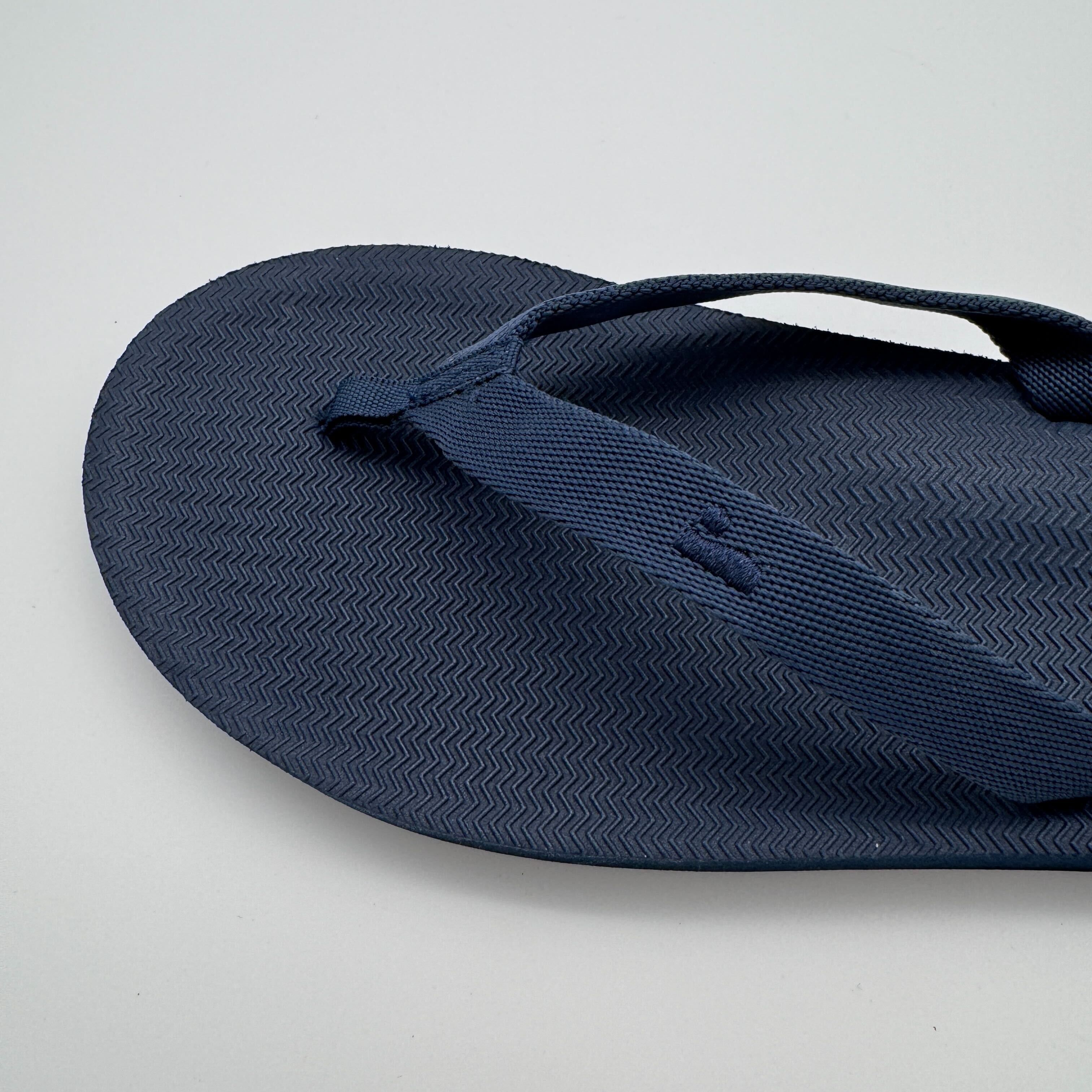 Blauer Flip-Flop-Sandale auf grauem Hintergrund, mit strukturiertem Fußbett und Riemen.