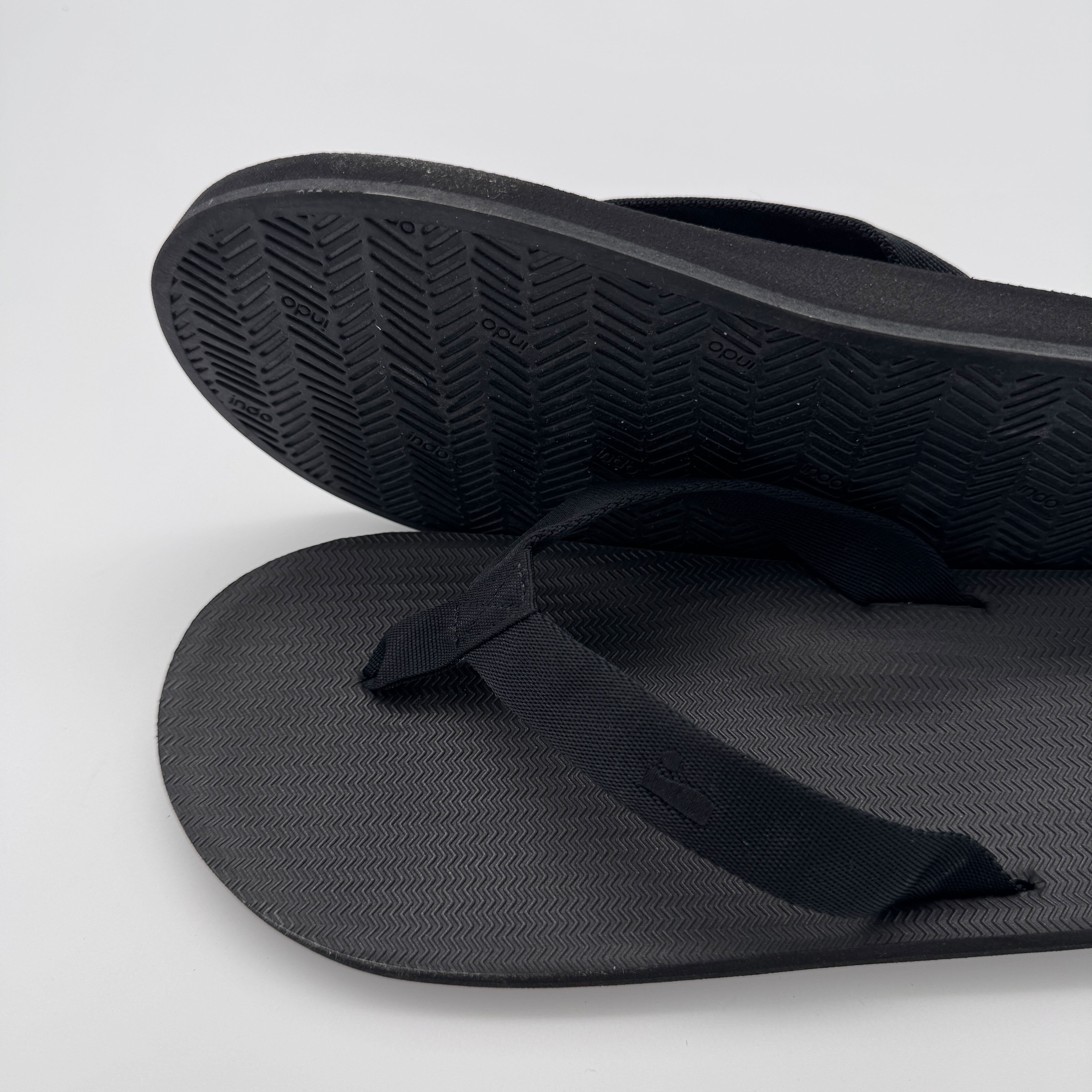 Schwarze Flip-Flops liegen aufeinander, wobei die Sohle eines Schuhs sichtbar ist.