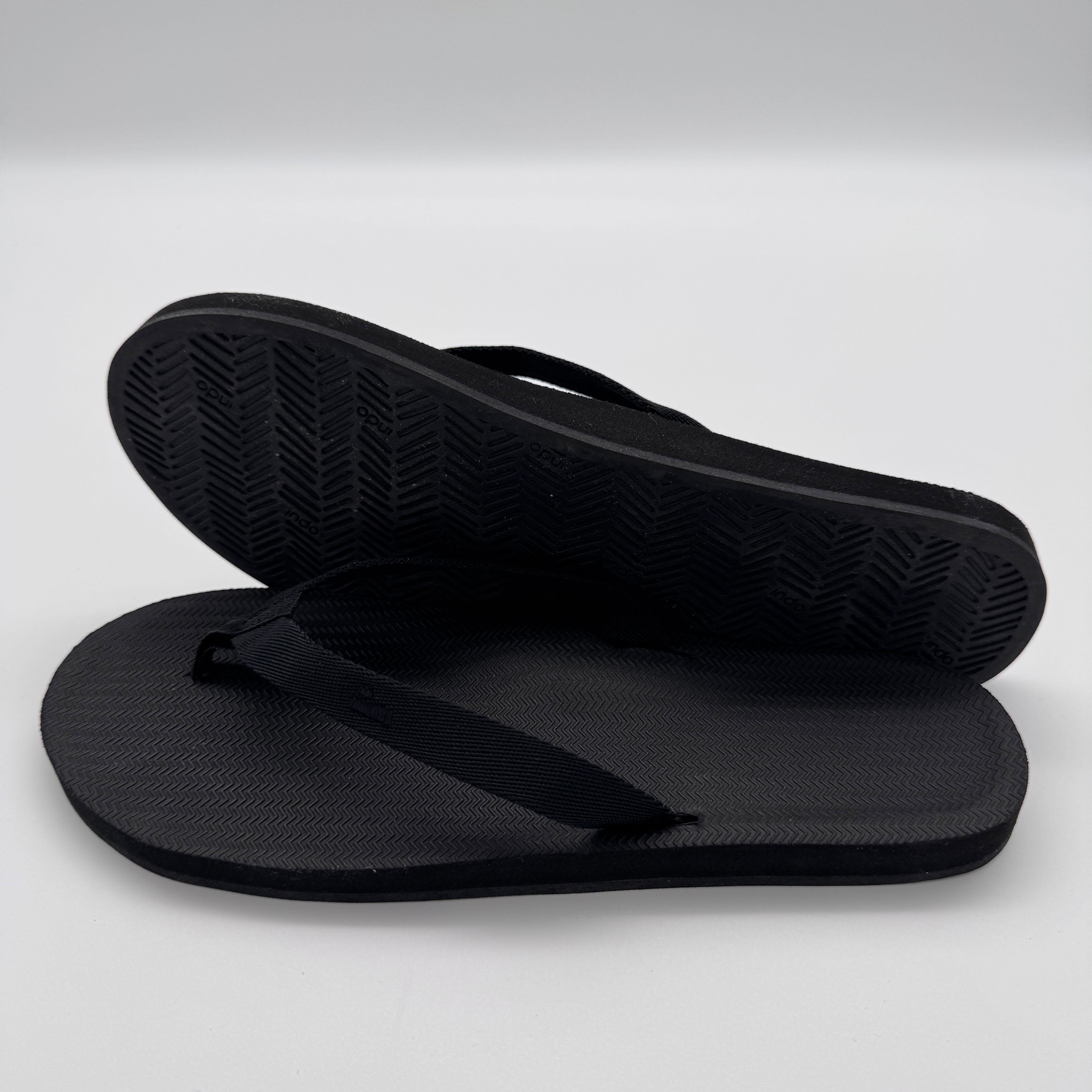 Ein Paar schwarze Flip-Flops, eines aufrecht stehend und das andere flach liegend, mit weißen Hintergrund.