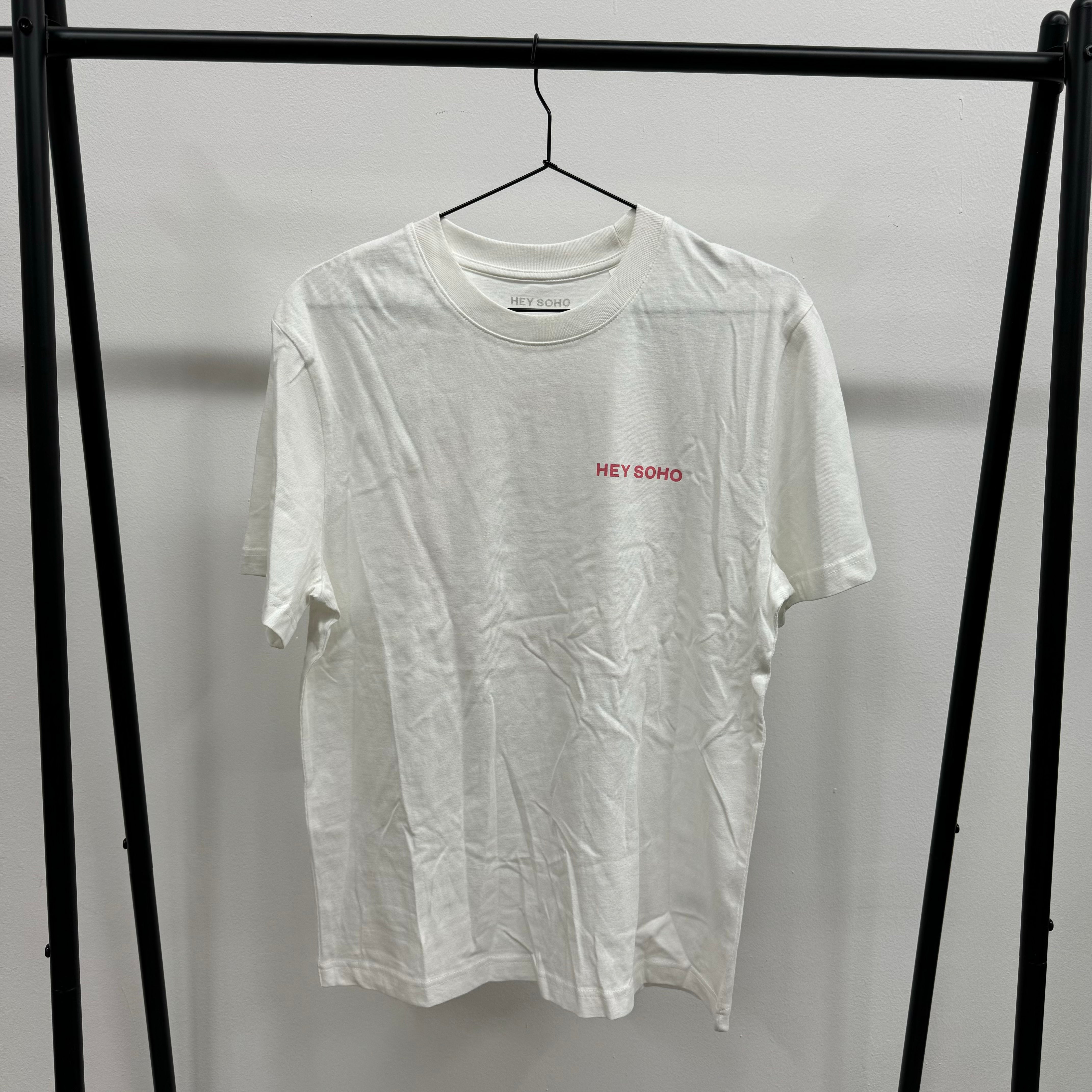 Weißes T-Shirt mit dem roten Text "HEY SOHO", das an einem schwarzen Kleiderbügel hängt.