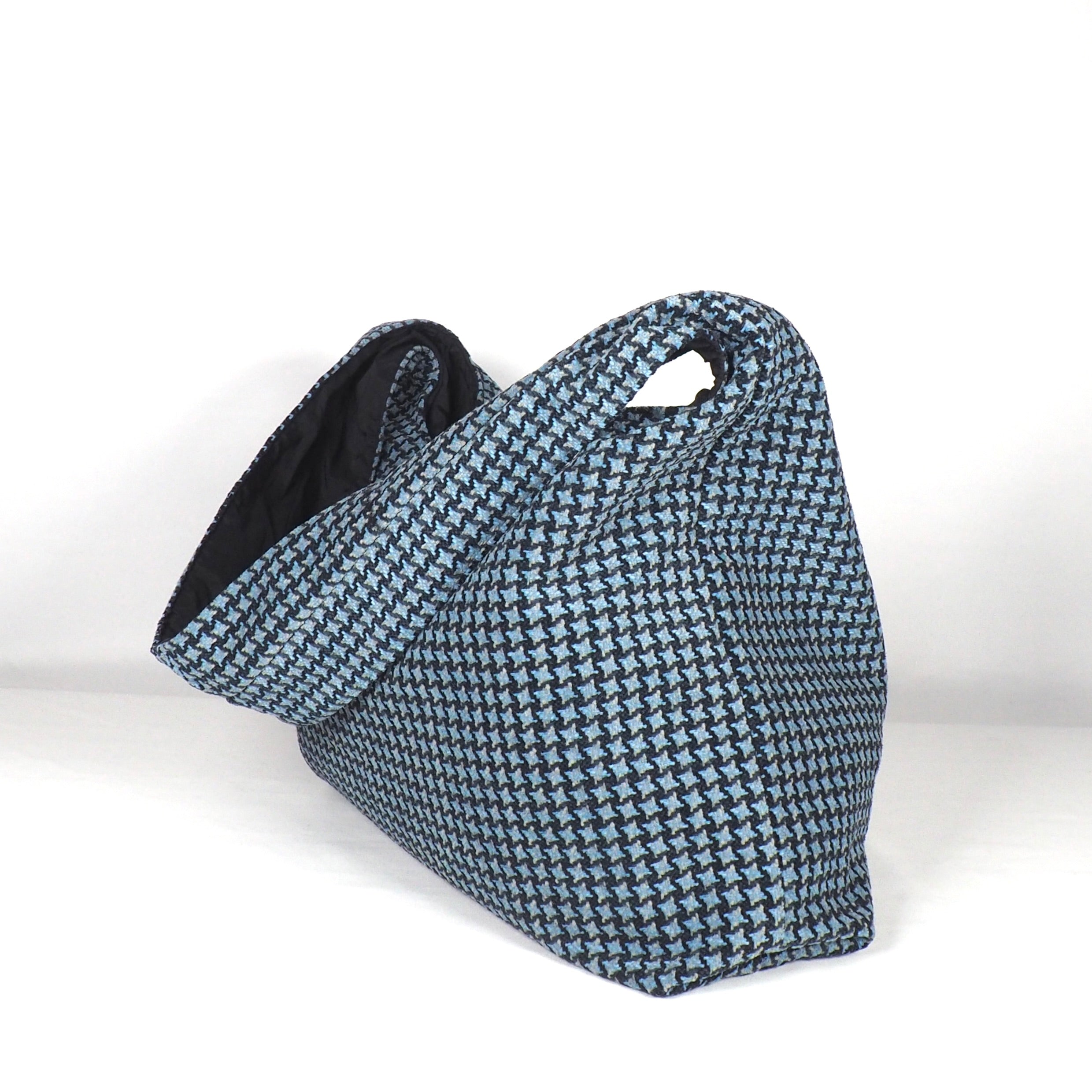 Eine weiche Stofftasche mit blau-schwarzem Hahnentrittmuster, zwei Henkeln und einem geräumigen, bequemen Design, fotografiert vor einem schlichten weißen Hintergrund.