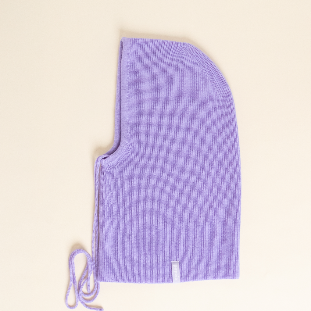 Lila gestrickte Balaklava mit Kordeln, flach auf einem cremefarbenen Hintergrund liegend.