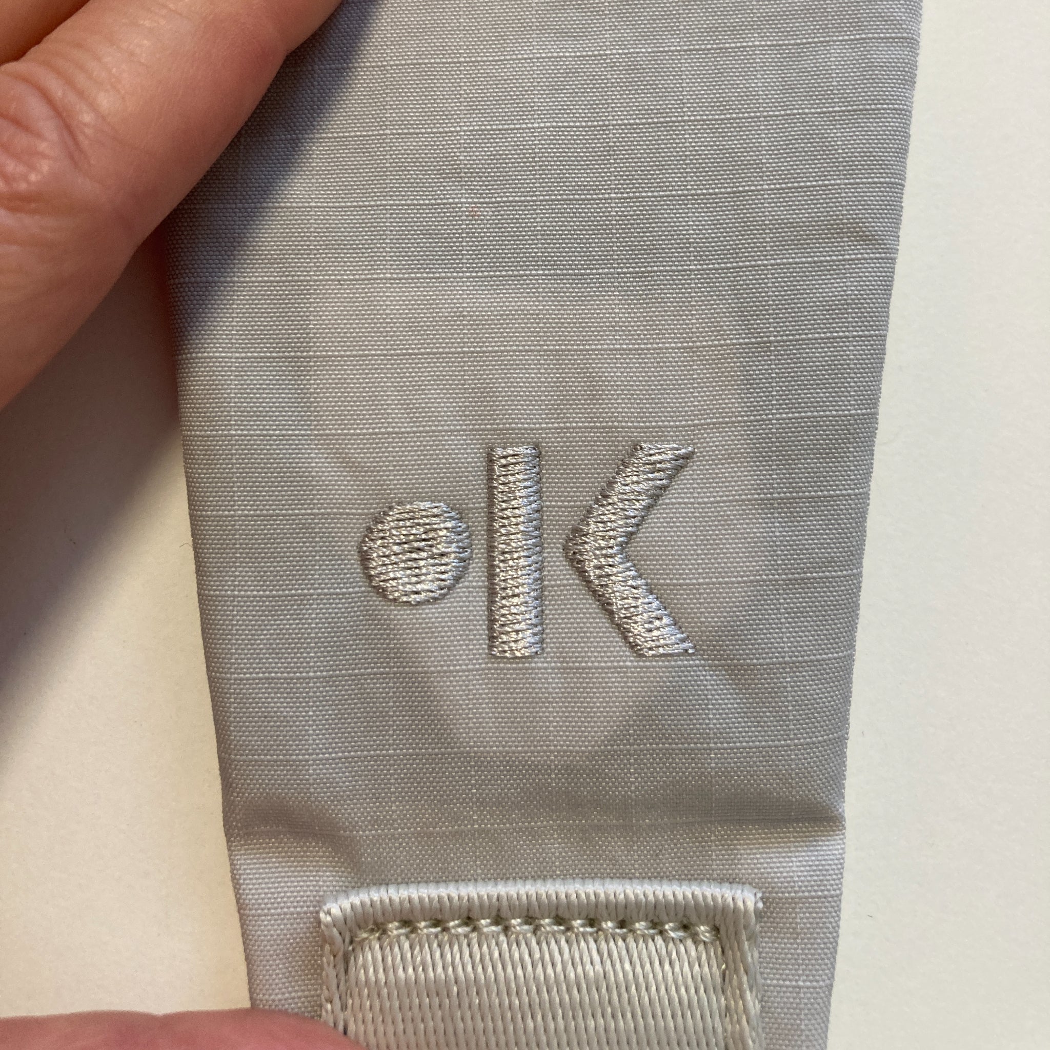 Nahaufnahme eines grauen Stoffstücks mit einem eingestickten Punkt und dem Buchstaben "K".