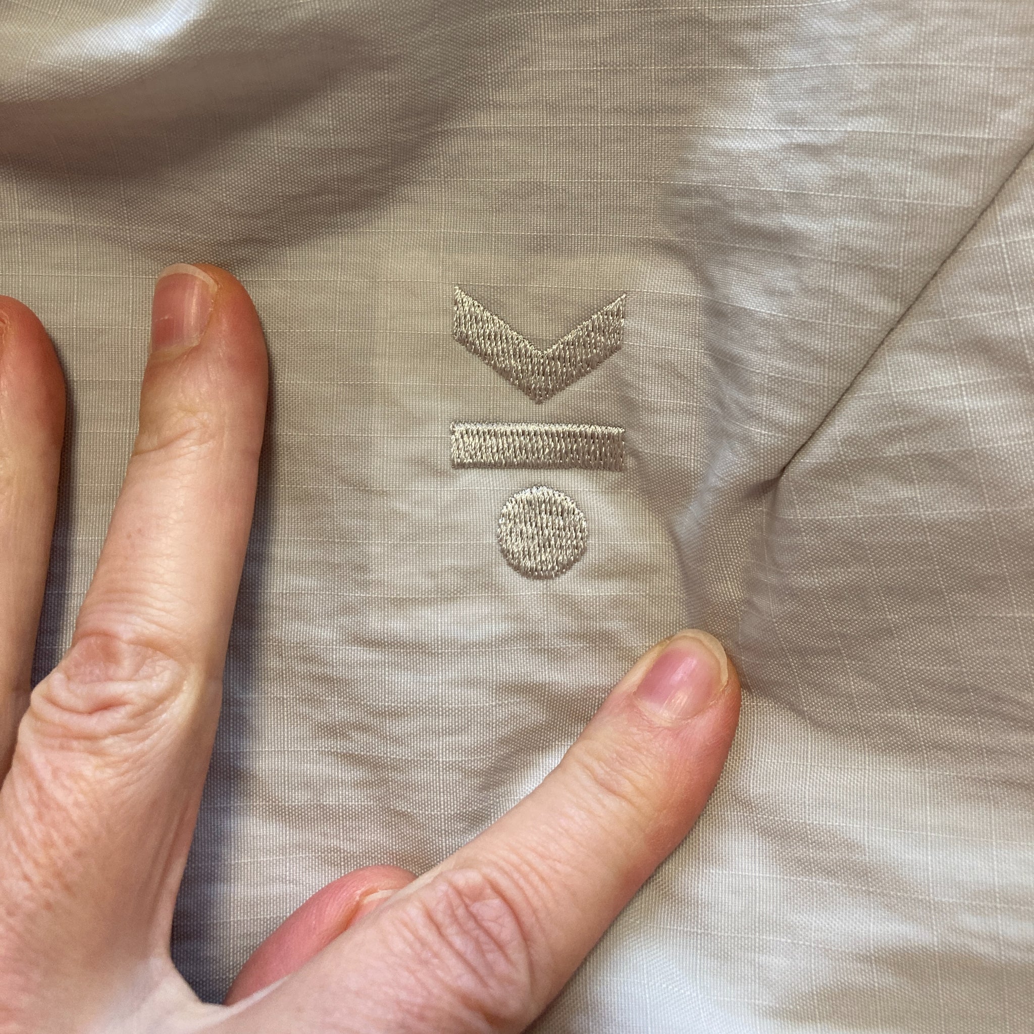 Hand berührt Stoff mit aufgesticktem Symbol aus zwei Pfeilen und einem Punkt auf einem Balken.