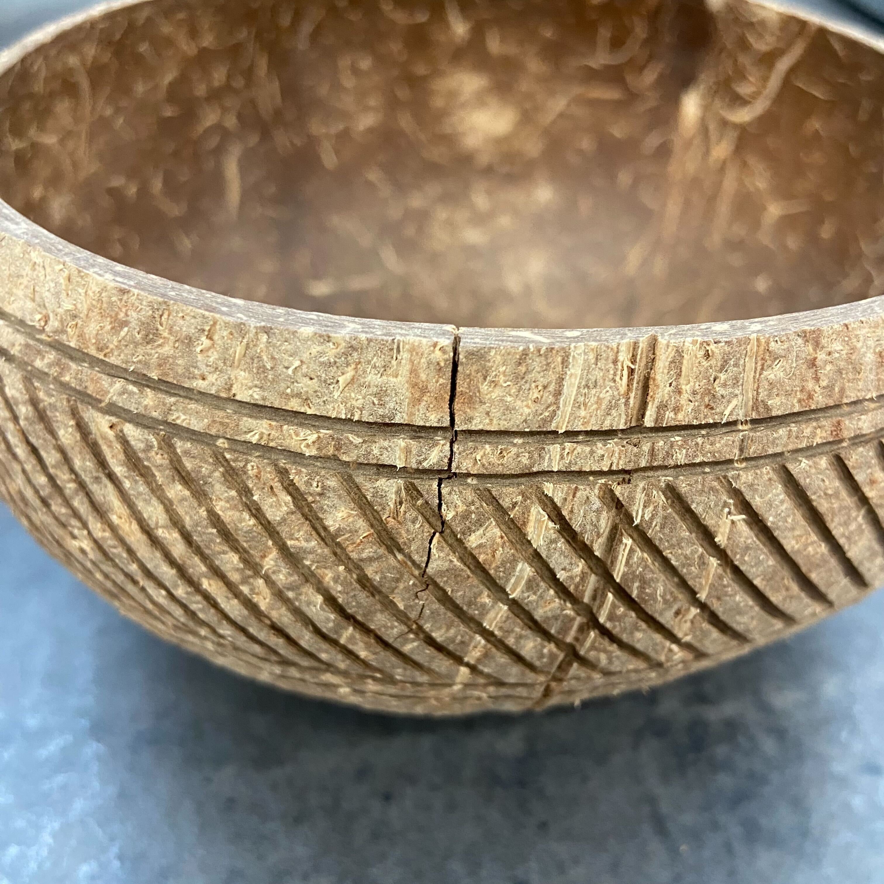 Nahaufnahme einer Schale aus Kokosnussschale mit eingraviertem Muster und einem sichtbaren Riss auf der Oberfläche.