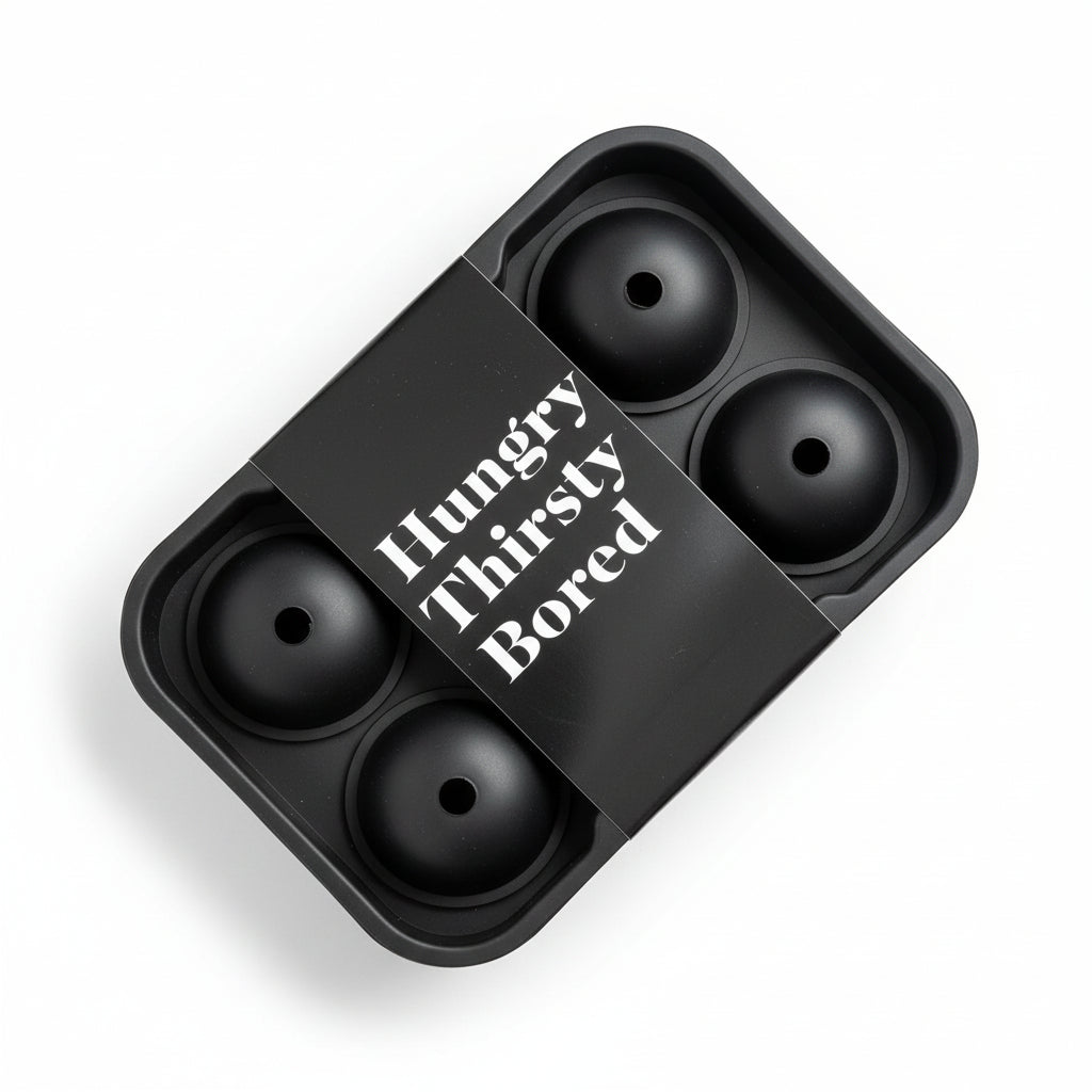 Eine schwarze Silikonform für Eiskugeln steht auf einer hölzernen Unterlage, umhüllt von einem Etikett mit der Aufschrift "Hungrig/Durstig/Langweilig" in weißer Schrift.