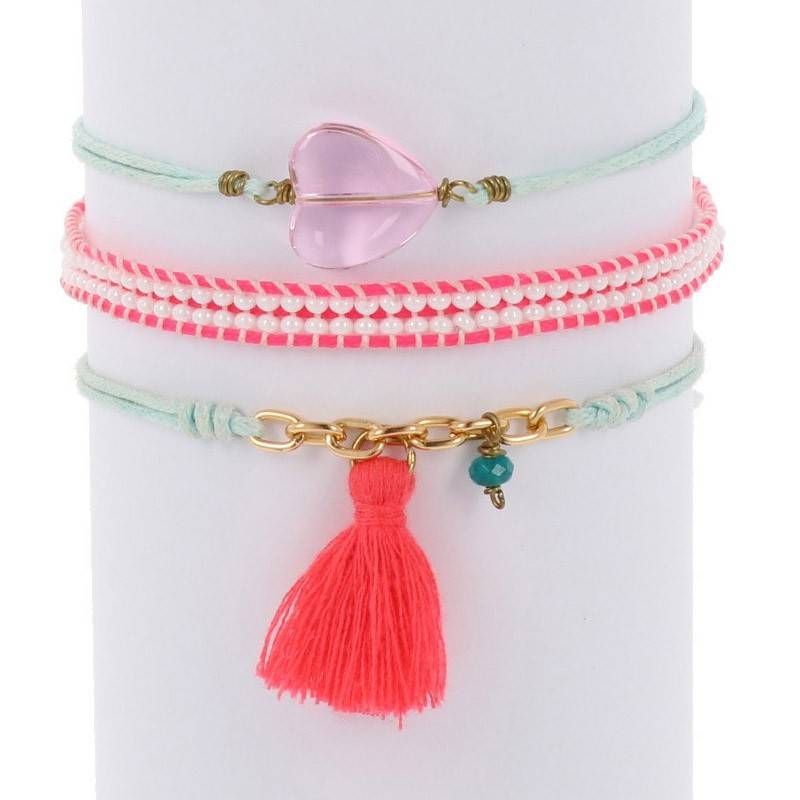 Drei pastellfarbene Armbänder: das obere mit einer rosafarbenen Herzperle, das mittlere mit kleinen rosafarbenen und weißen Perlen und das untere mit einer goldenen Kette, einer winzigen blaugrünen Perle und einer leuchtend rosafarbenen Quaste, alles auf einem weißen zylindrischen Ständer.