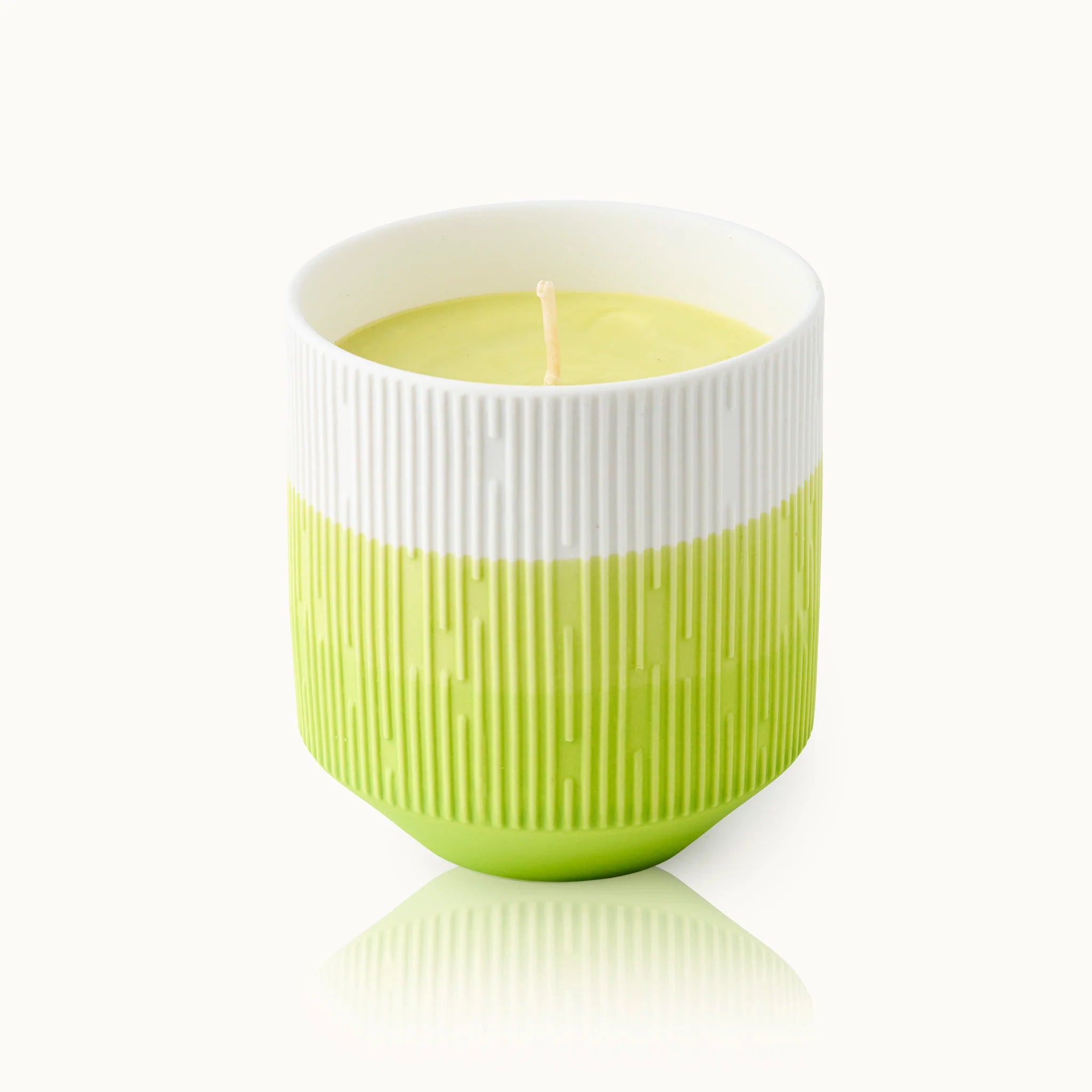 Grüne und weiße Kerze in einem strukturierten Gefäß mit einem zentralen Docht, auf hellem Hintergrund.