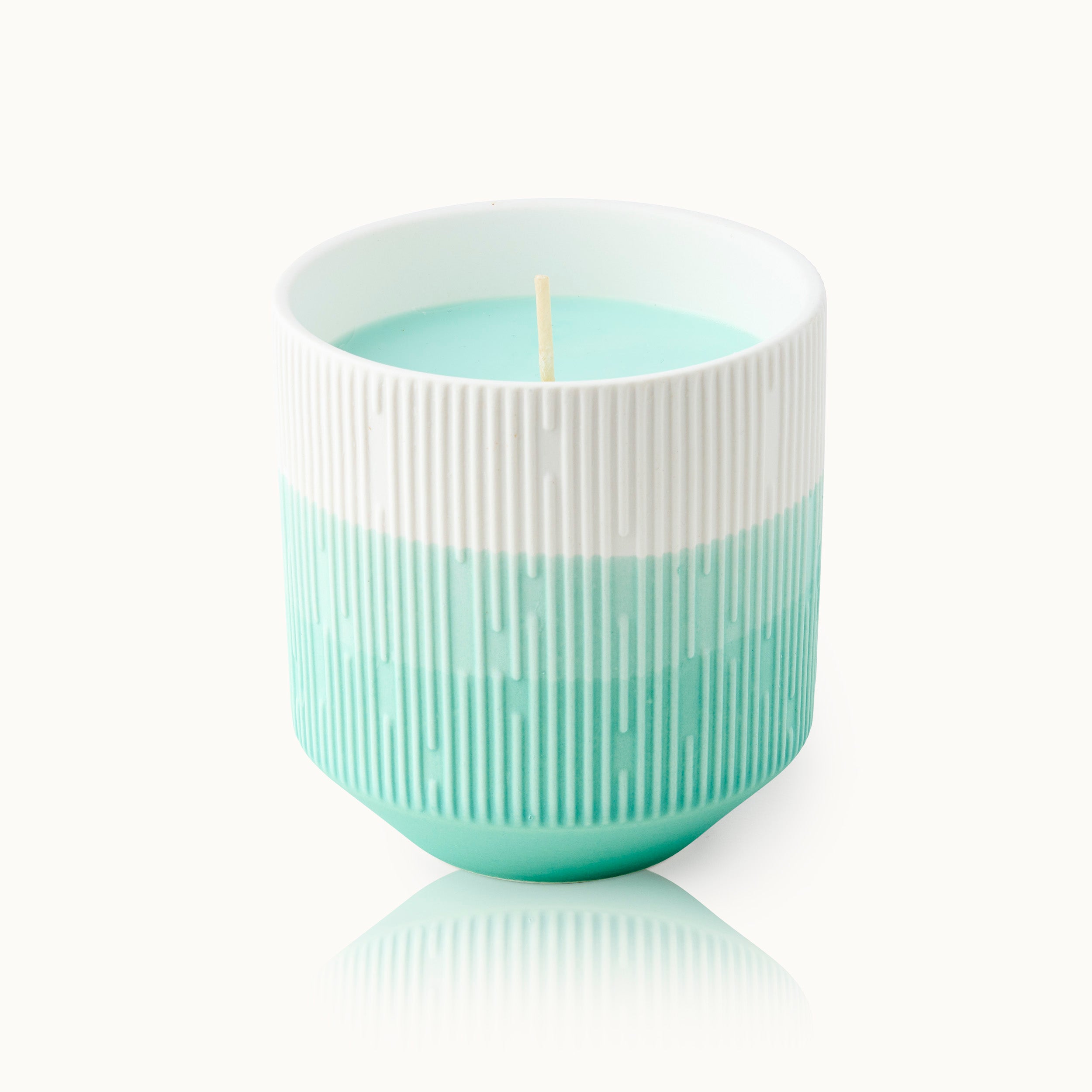 Aqua-weiße Kerze in einem gerippten, zweifarbigen Keramikbehälter mit reflektierender Basis.