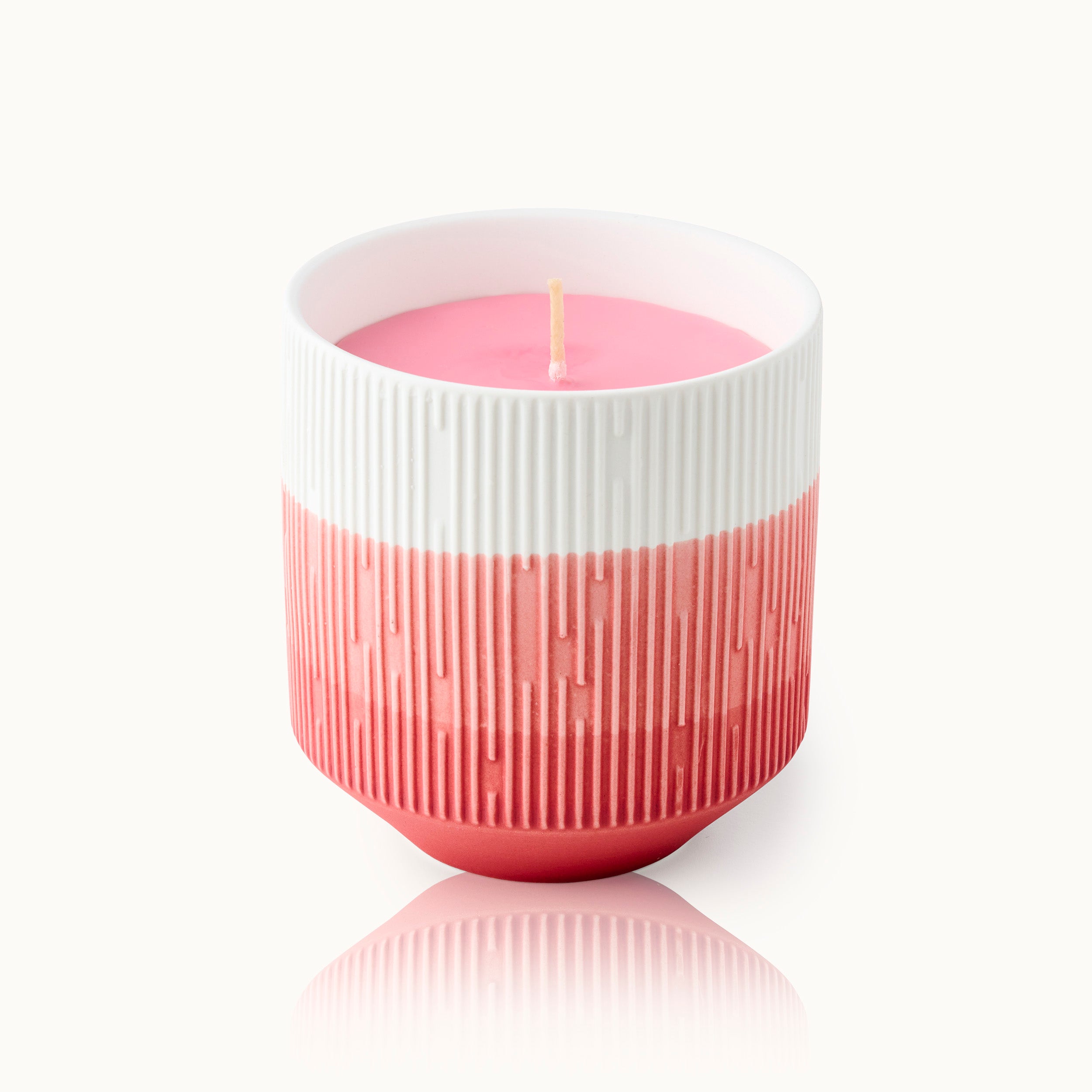 Rosa Kerze in einem rot-weiß gestreiften, geriffelten Keramikbehälter, auf weißem Hintergrund.