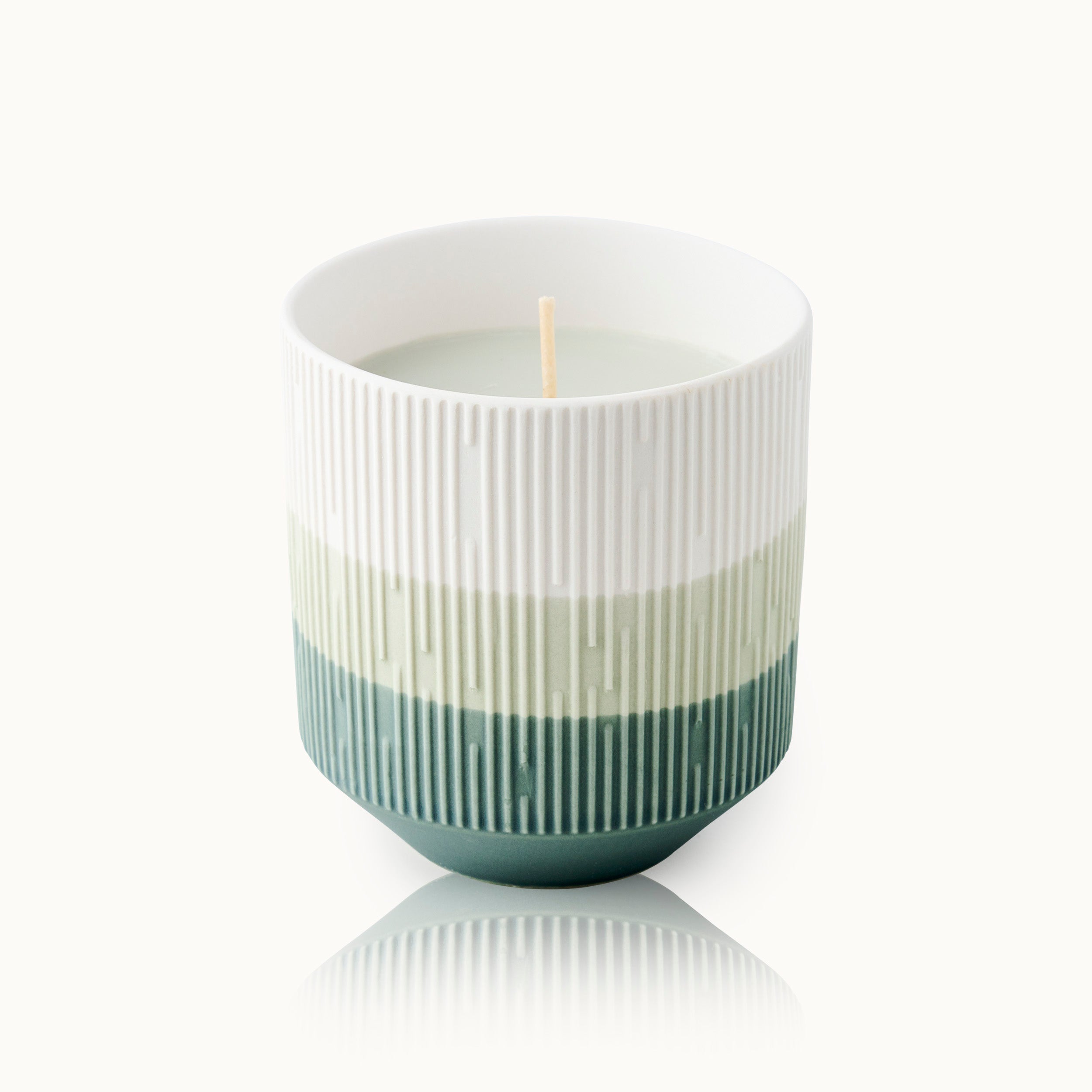 Weiße Kerze in einem gerippten, mehrfarbigen Keramikbecher mit Grüntönen.
