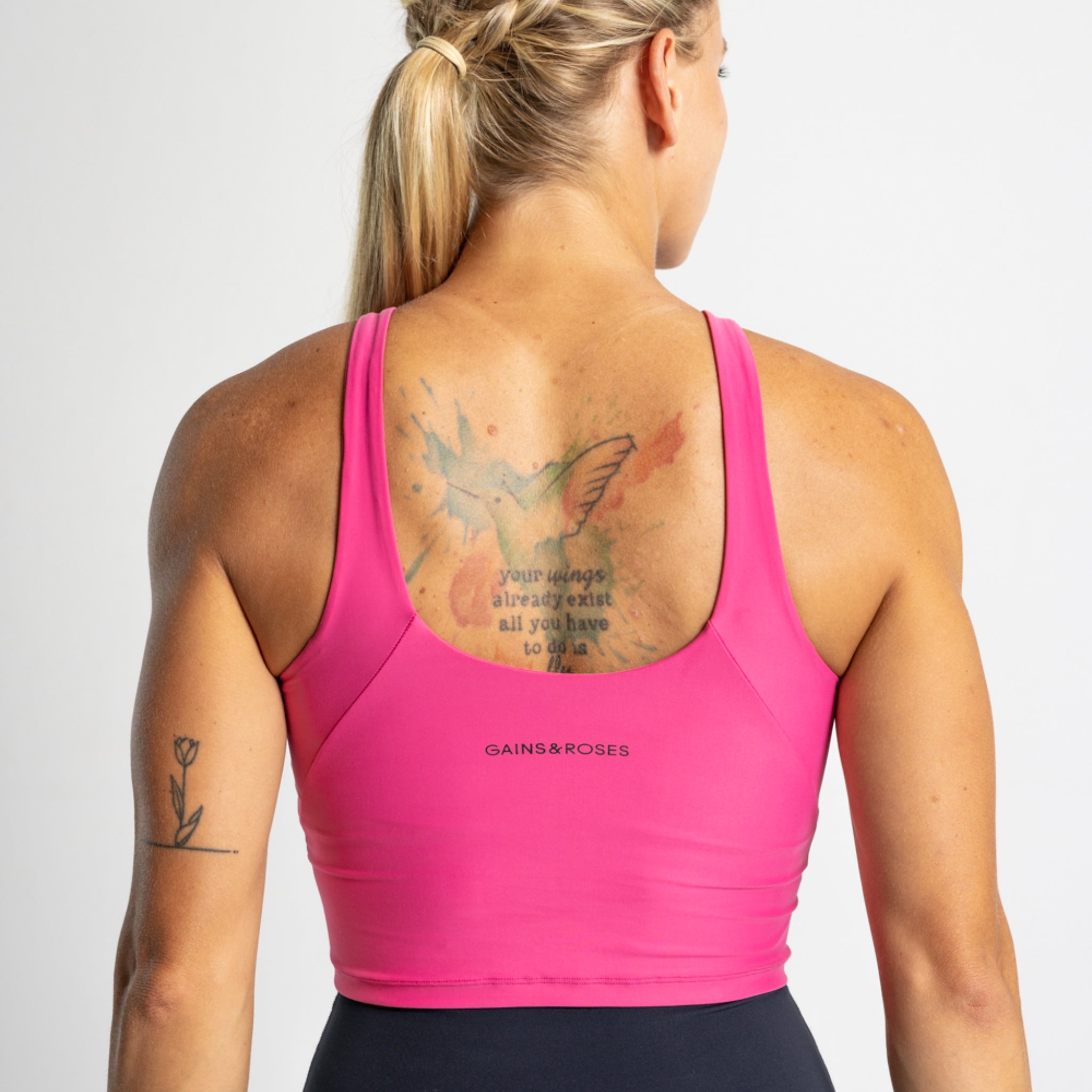 Frau von hinten in einem pinken Sporttop mit Tattoos auf Rücken und Arm.