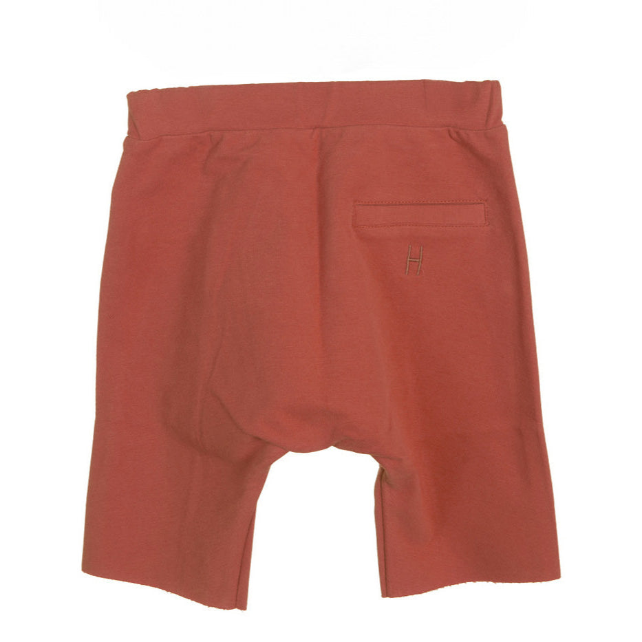 Rote Shorts mit einem elastischen Bund und einer einzigen Gesäßtasche auf der rechten Seite. Der Saum ist gerade geschnitten, und in der Nähe der Tasche befindet sich ein kleines genähtes Muster. Die Shorts liegen flach auf einem weißen Hintergrund.