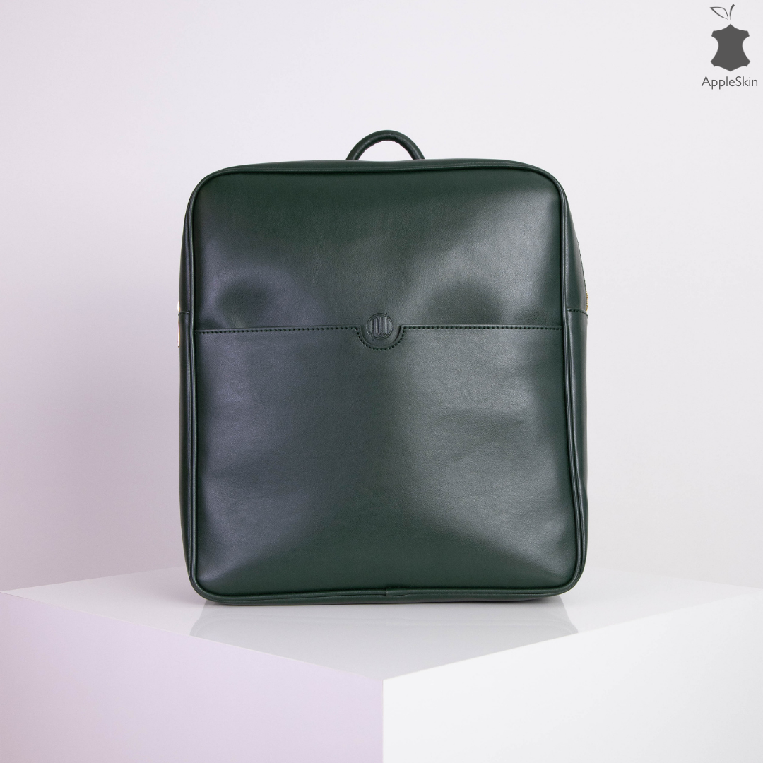 Ein eleganter, dunkelgrüner Rucksack aus Lederimitat steht auf einem weißen Podest vor einem schlichten Hintergrund.