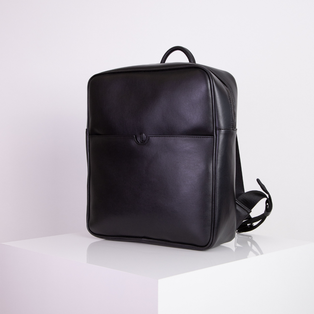 Schwarzer Lederrucksack auf weißem Sockel, seitlich ausgerichtet in minimalistischem Stil.