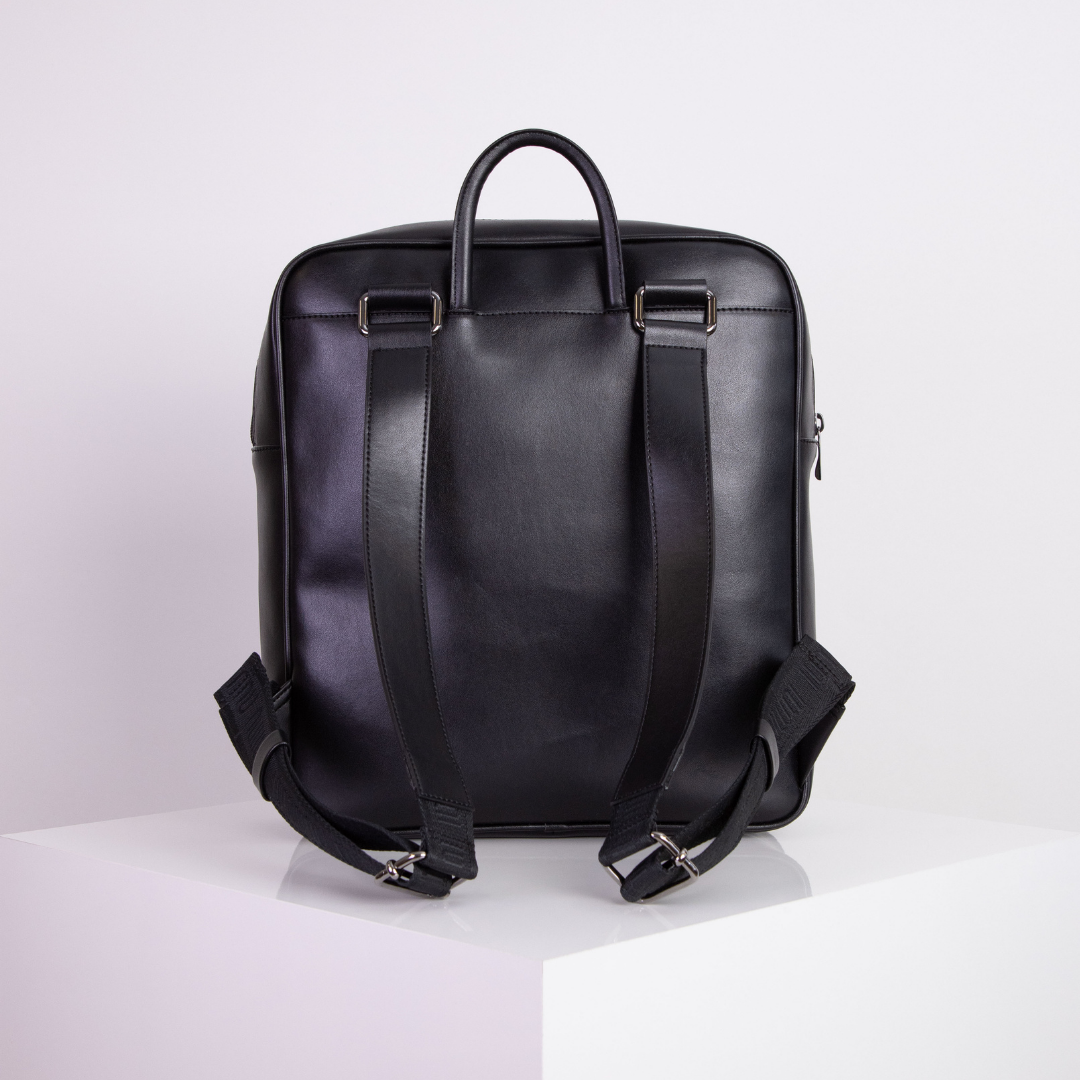 Schwarzer Lederrucksack auf einem weißen Podest vor einem neutralen Hintergrund.