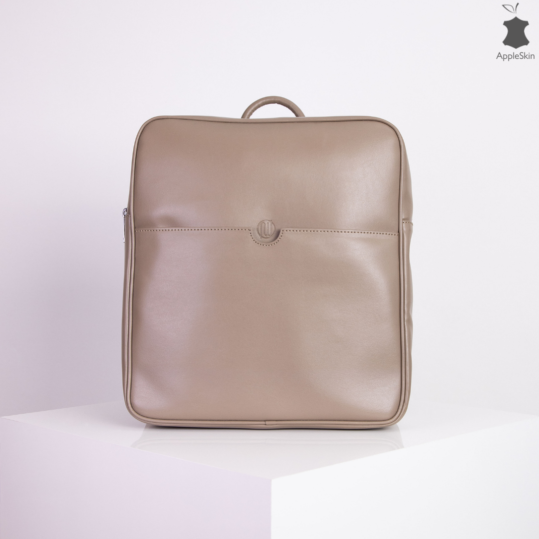 Beigefarbener Rucksack aus glattem Material auf einem weißen Tisch vor weißem Hintergrund.