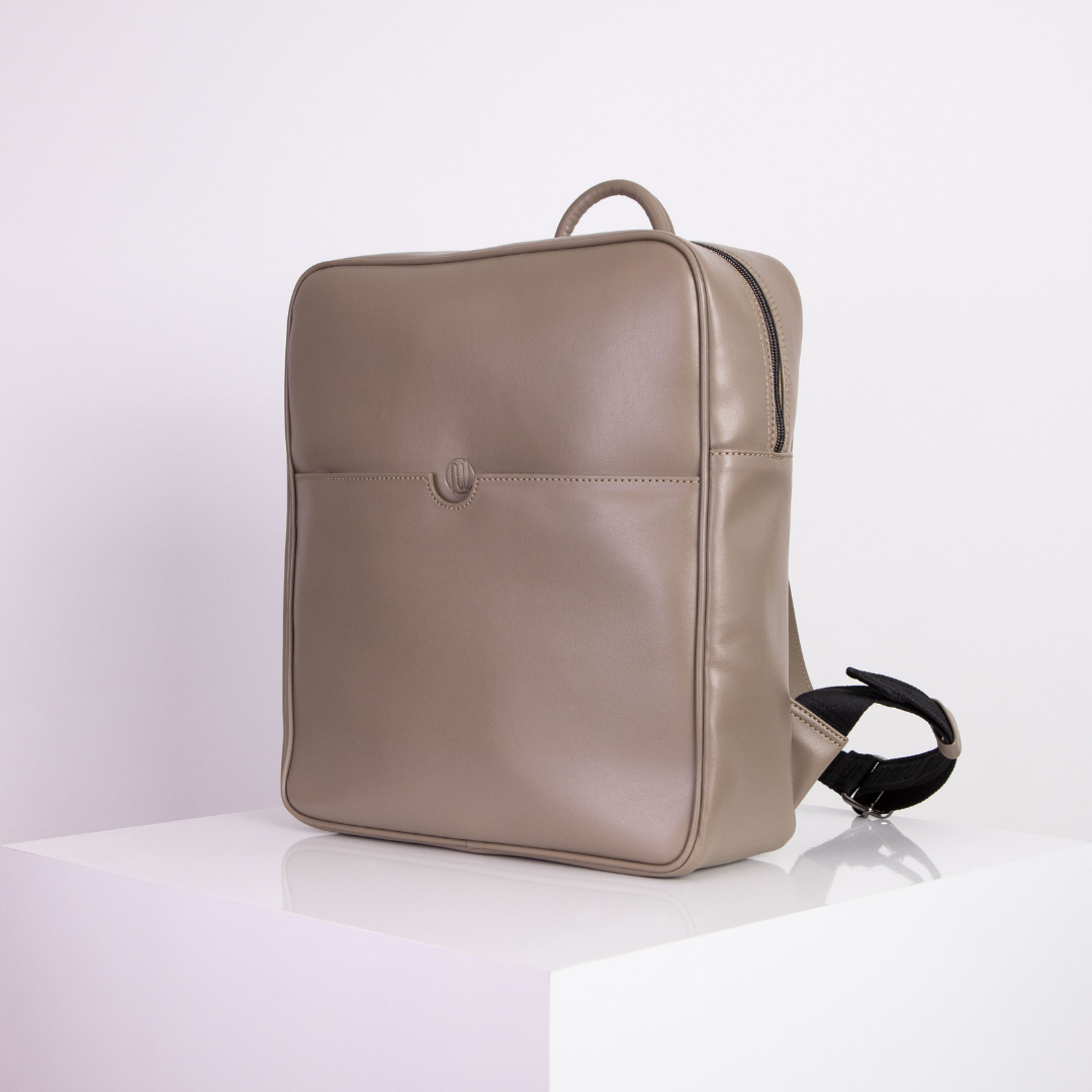 Beigefarbener, quadratischer Rucksack steht auf einem weißen Tisch vor einem neutralen Hintergrund.