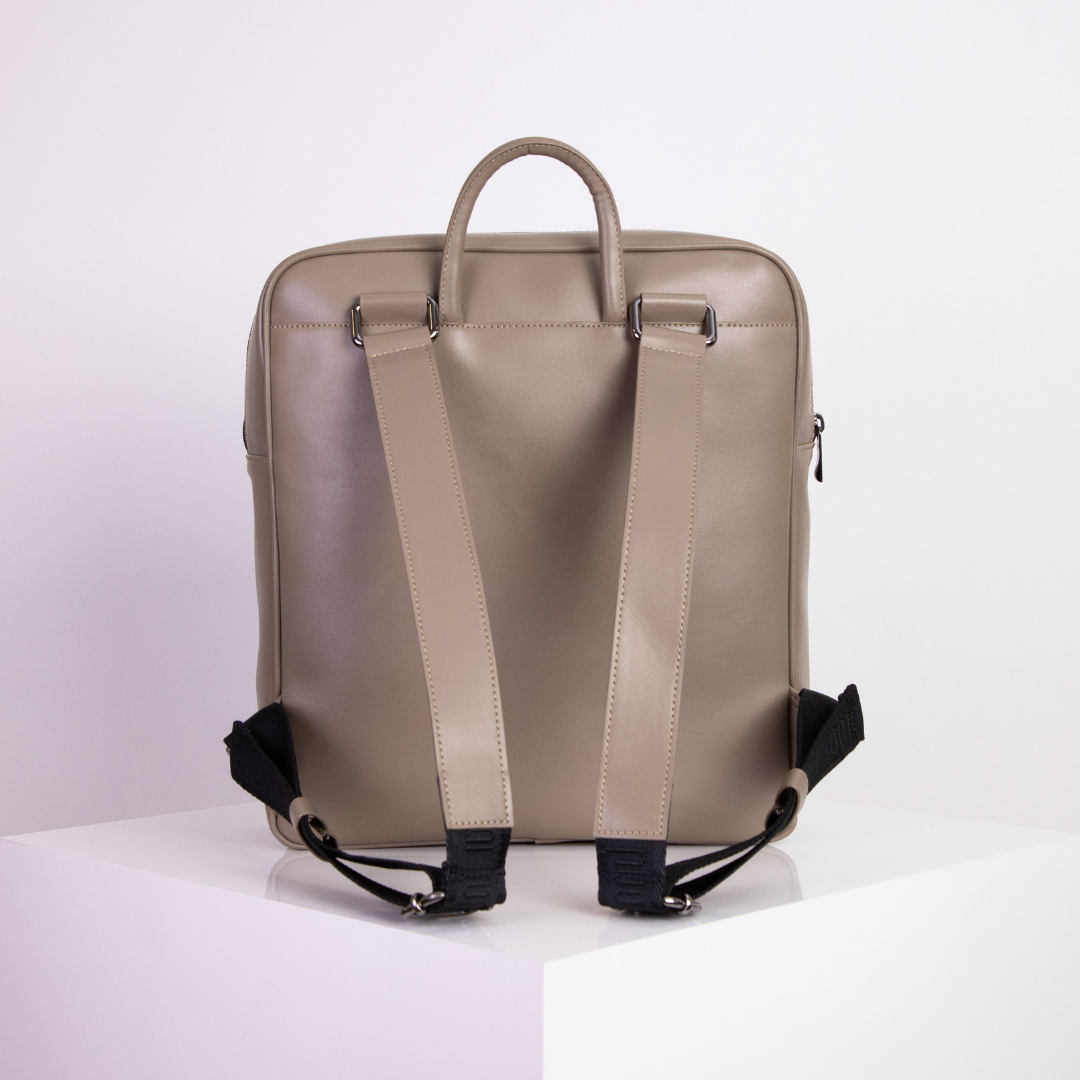 Beiger Rucksack mit Tragegriffen und Schultergurten, auf einem weißen Podest stehend.