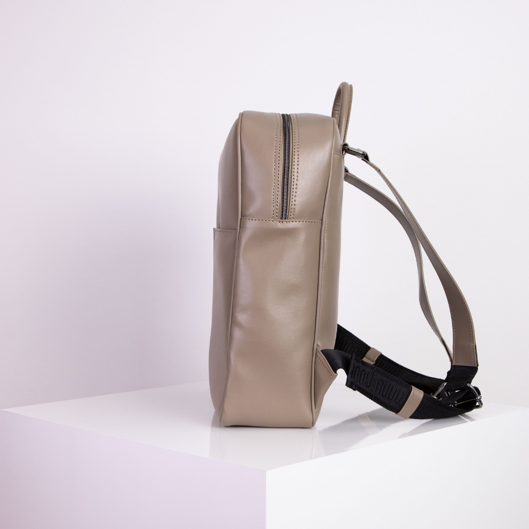 Beiger Rucksack in Seitenansicht auf einem weißen Podest vor hellem Hintergrund.