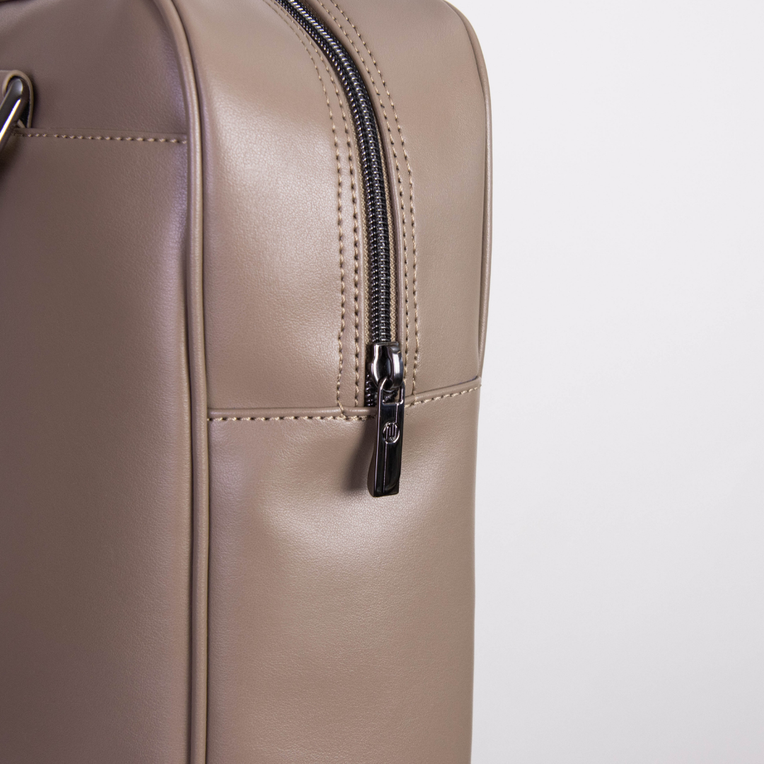 Nahaufnahme eines beigen Lederkoffers mit einem silbernen Reißverschluss und sichtbaren Nähten.