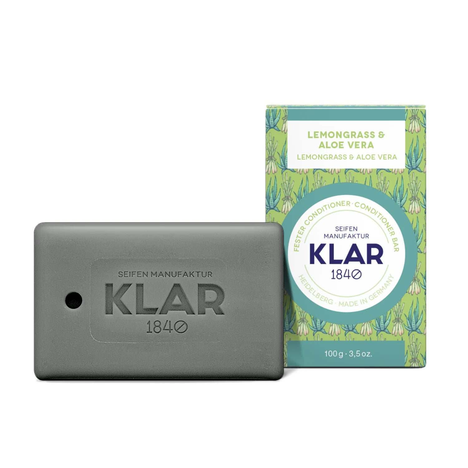 Ein rechteckiges graues Seifenstück mit der Aufschrift KLAR 1840 steht neben der dekorativen grünen Schachtel mit der Aufschrift Lemongrass & Aloe Vera, Conditioner Bar, Made in Germany, 100g.