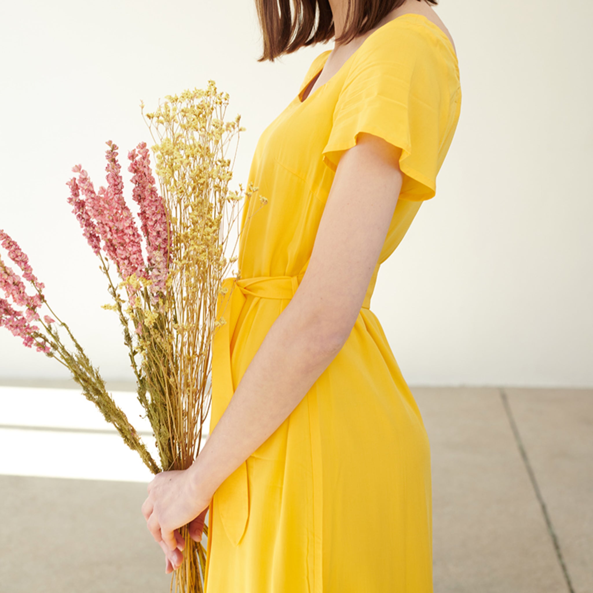 Frau im gelben Kleid hält einen Strauß Trockenblumen in den Händen.