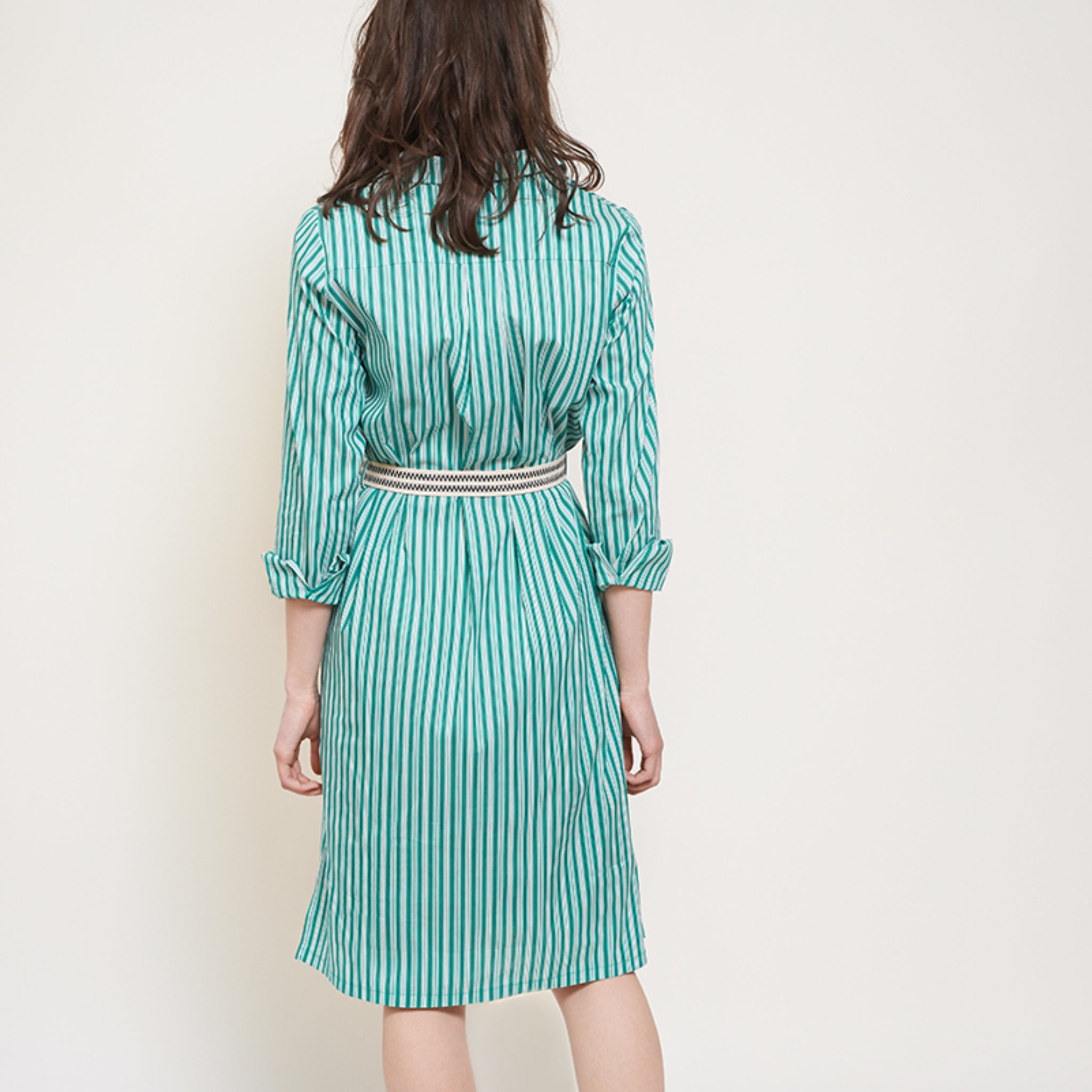 Eine Frau trägt ein blau-grün gestreiftes Kleid mit Gürtel und steht mit dem Rücken zur Kamera.